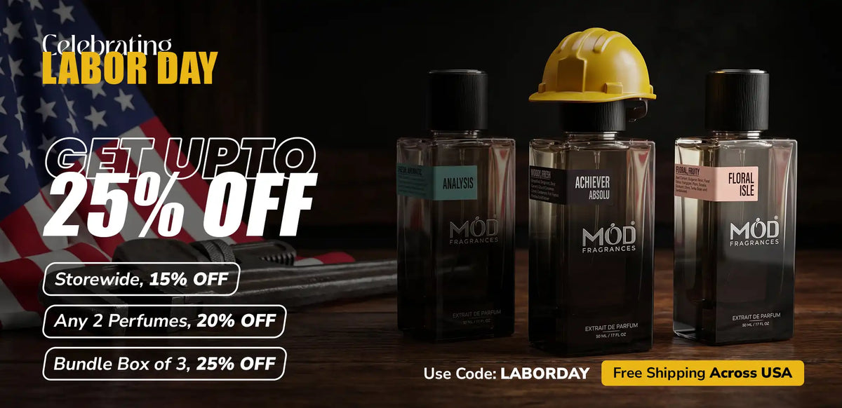 Promotional Labor Day advertisement showing three perfume bottles from MOD Perfumes on a dark wooden surface with an American flag in the background. Large text advertises up to 25% off storewide and bundle deals, with a yellow hard hat on the middle bottle.