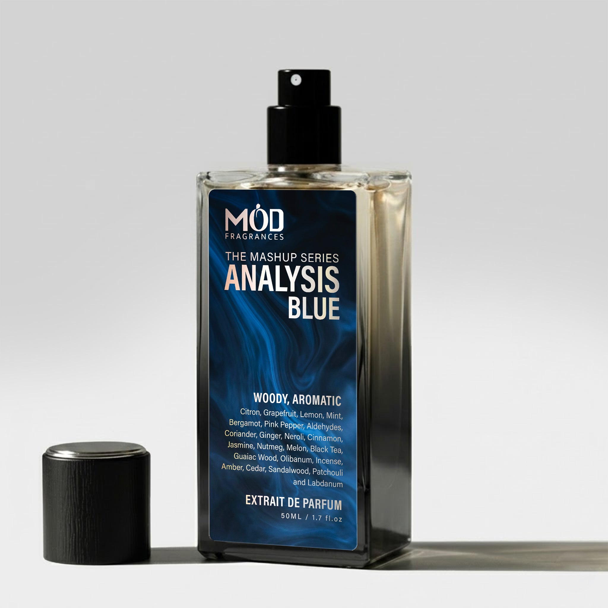 A rectangular glass perfume bottle by MOD Fragrances, labeled "Mashup series Analysis Blue" stands on a light surface with its black cap placed beside it.