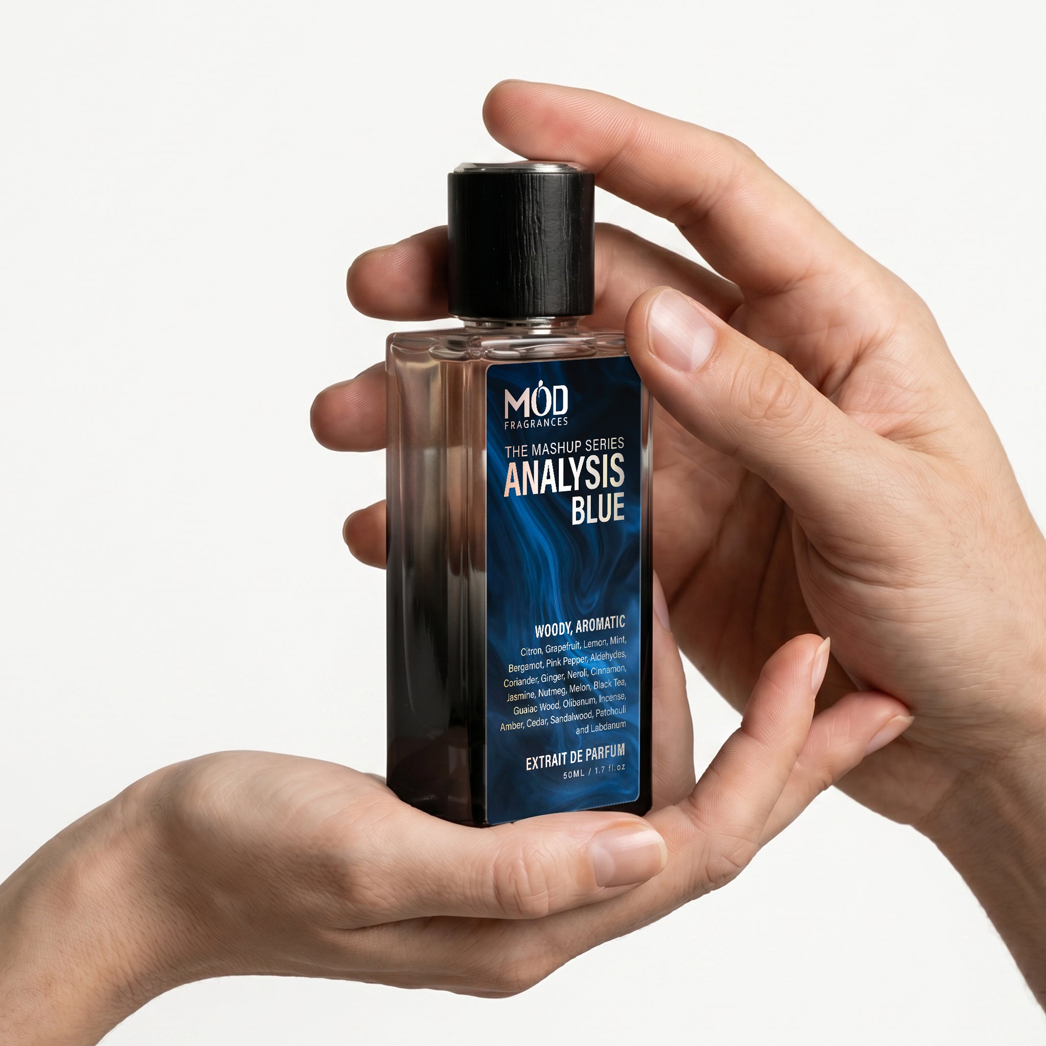 A person's hand holds a rectangular glass perfume bottle by MOD Fragrances, labeled "Mashup series Analysis Blue" against a plain white background.