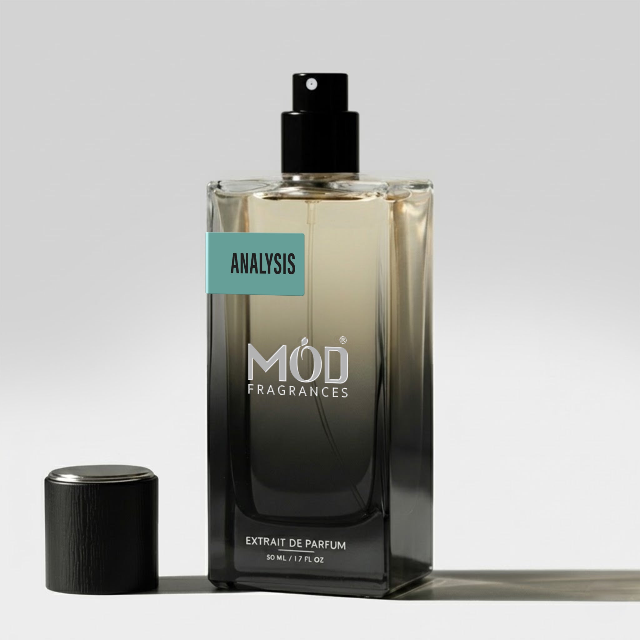 A rectangular glass perfume bottle by MOD Fragrances, labeled "Analysis" stands on a light surface with its black cap placed beside it.