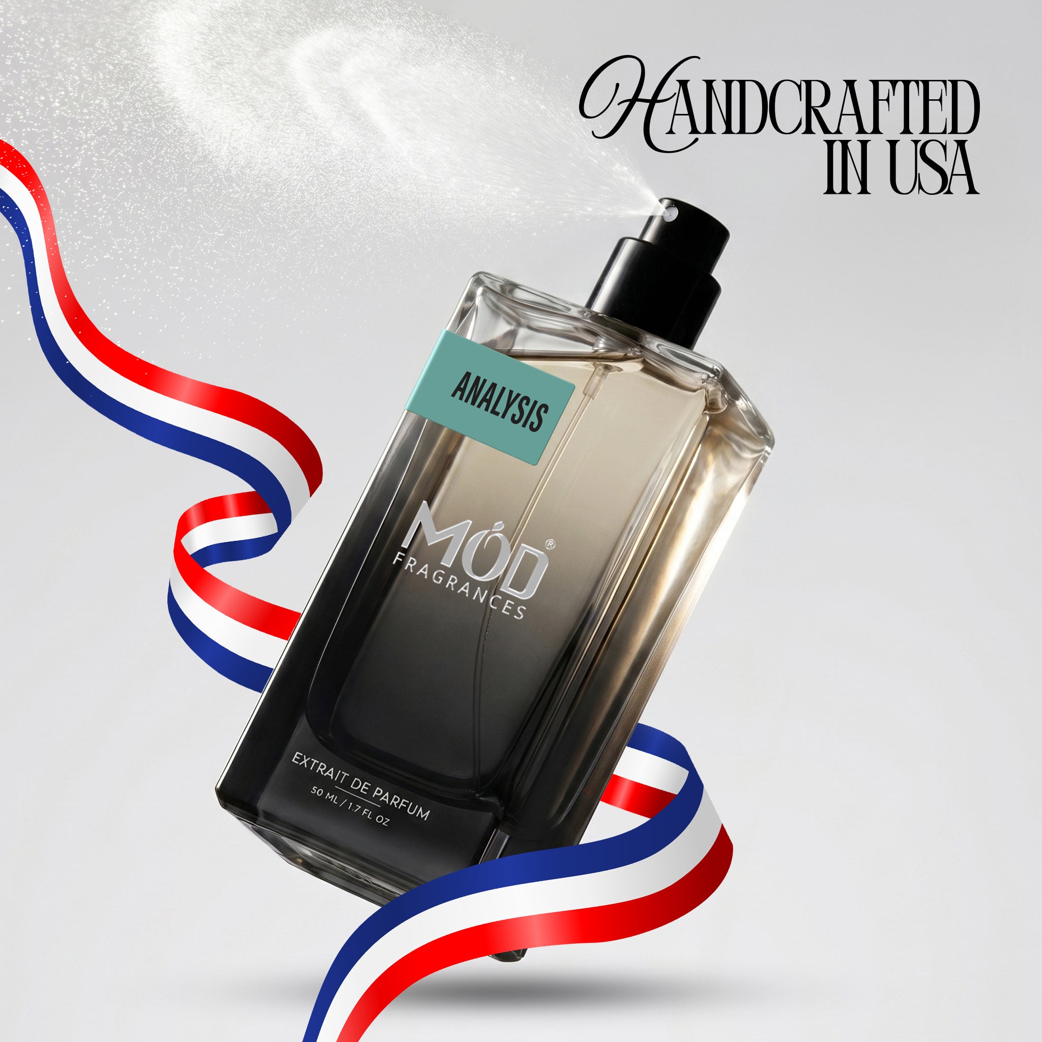 A rectangular glass perfume bottle by MOD Fragrances, labeled "Analysis" is captured mid-spray with a fine mist dispersing into the air, accented by stylized red, white, and blue ribbons, with the text "Handcrafted in USA" in the upper right.