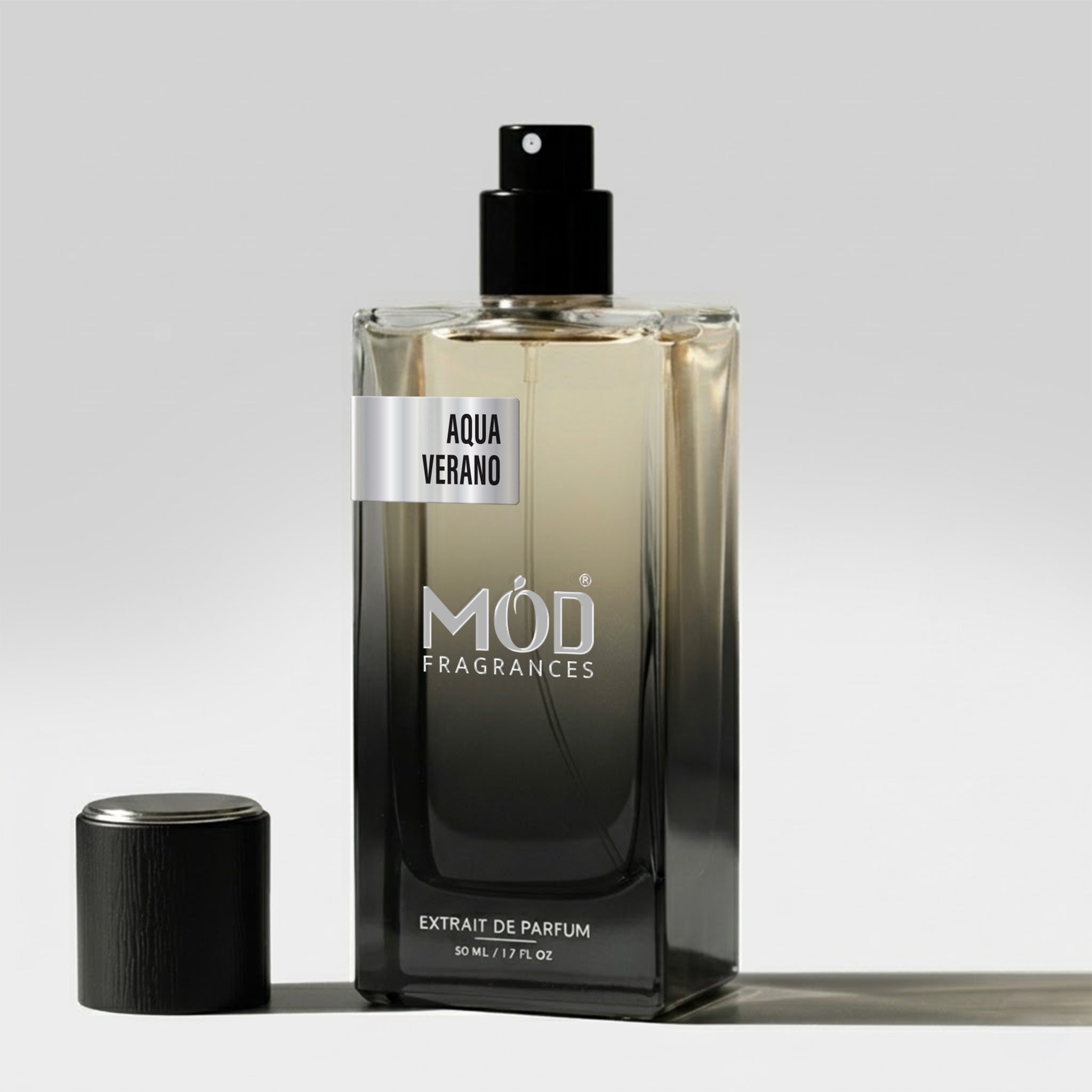 A rectangular glass perfume bottle by MOD Fragrances, labeled "Aqua Verano" stands on a light surface with its black cap placed beside it.
