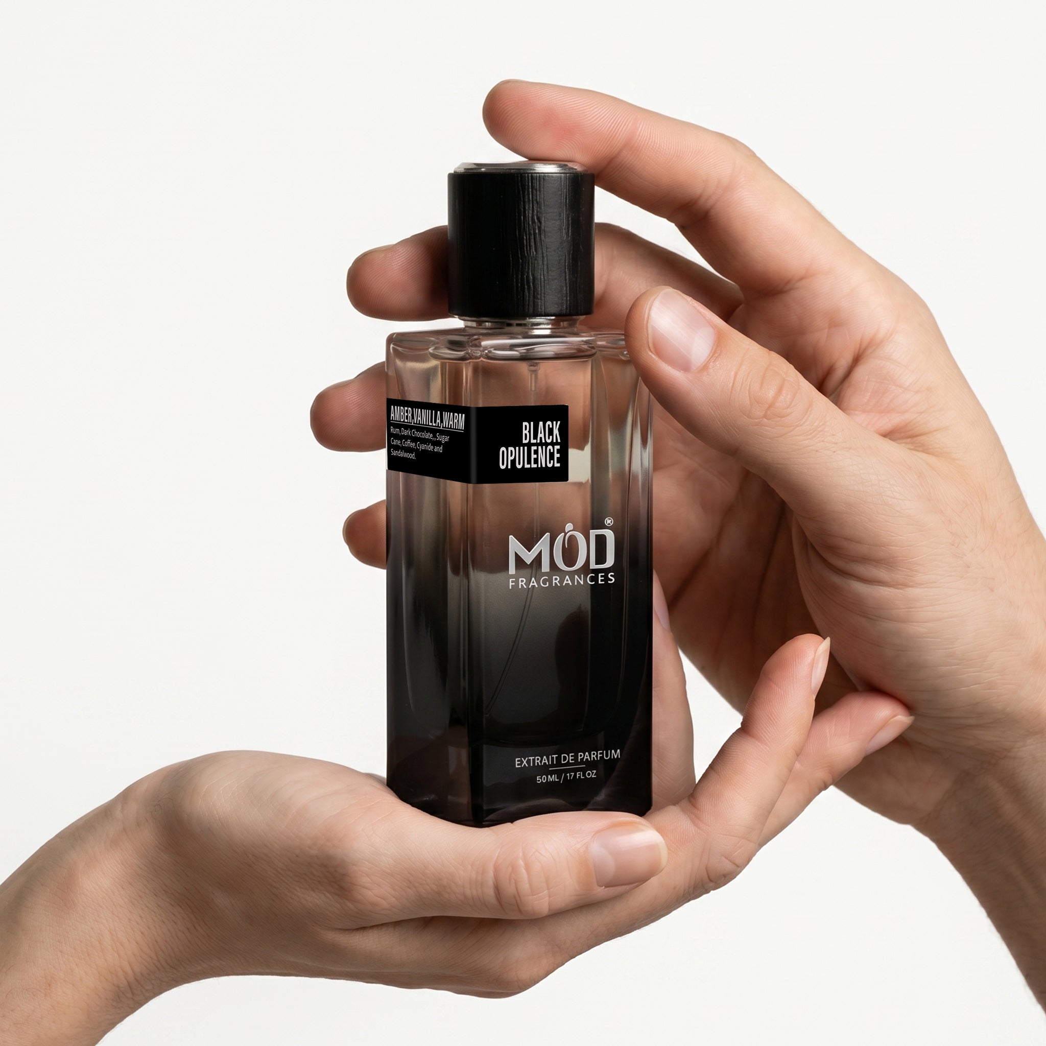 A male & Female person's hand holds a rectangular glass perfume bottle by MOD Fragrances, labeled "Black Opulence" against a plain white background.