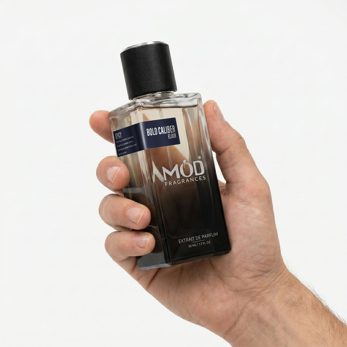 A Male person's hand holds a rectangular glass perfume bottle by MOD Fragrances, labeled "Bold Caliber Elixir” against a plain white background.