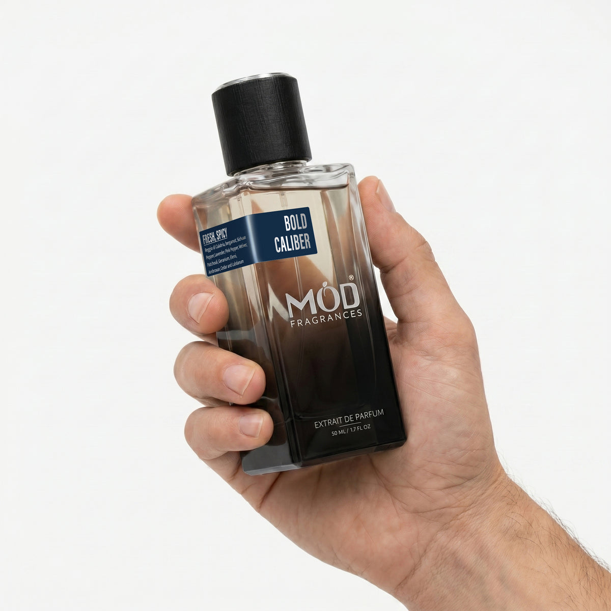 A Male person's hand holds a rectangular glass perfume bottle by MOD Fragrances, labeled "Bold Caliber” against a plain white background.
