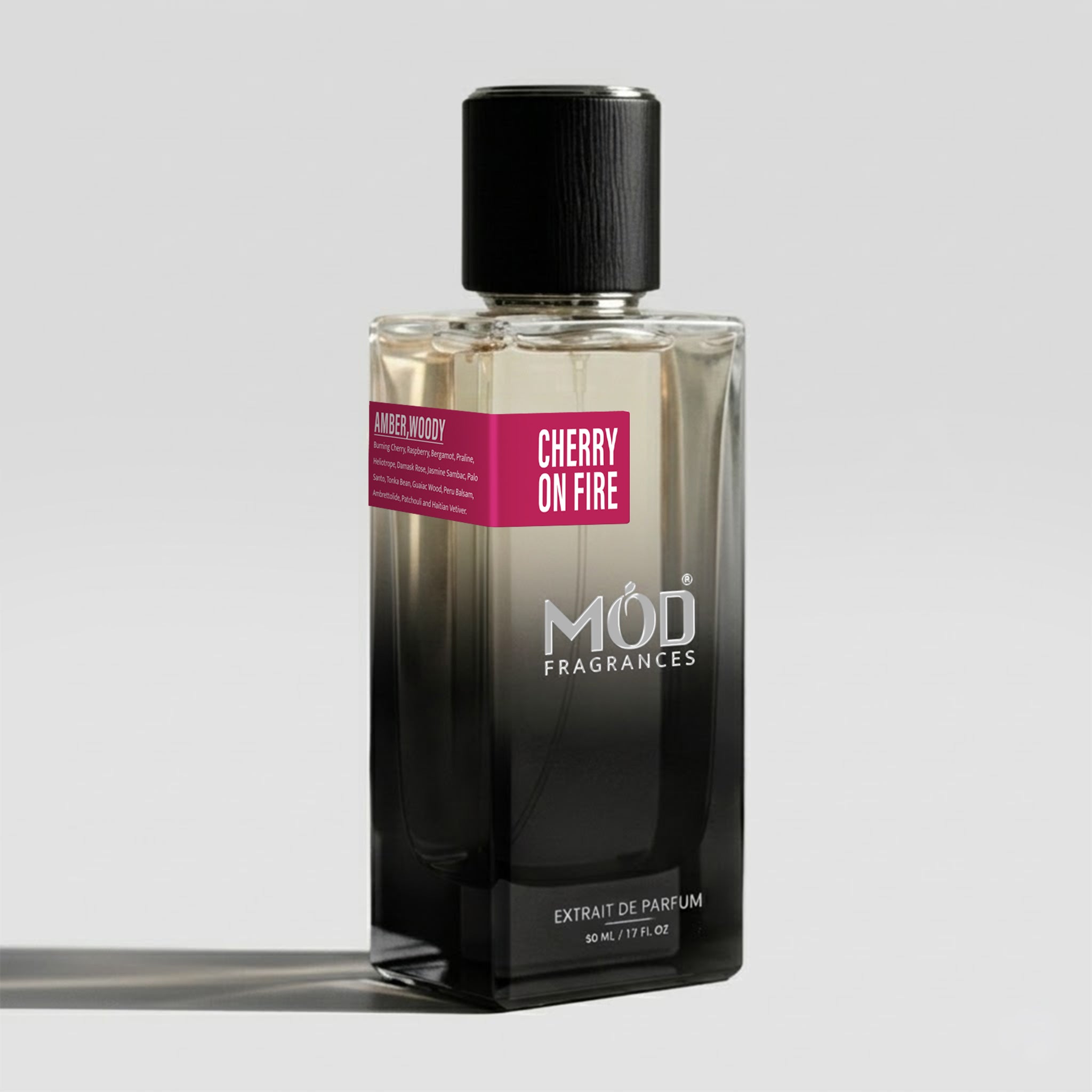 A rectangular glass perfume bottle by MOD Fragrances, labeled "Cherry on Fire" with a small label detailing its leather, woody notes, stands on a light background.