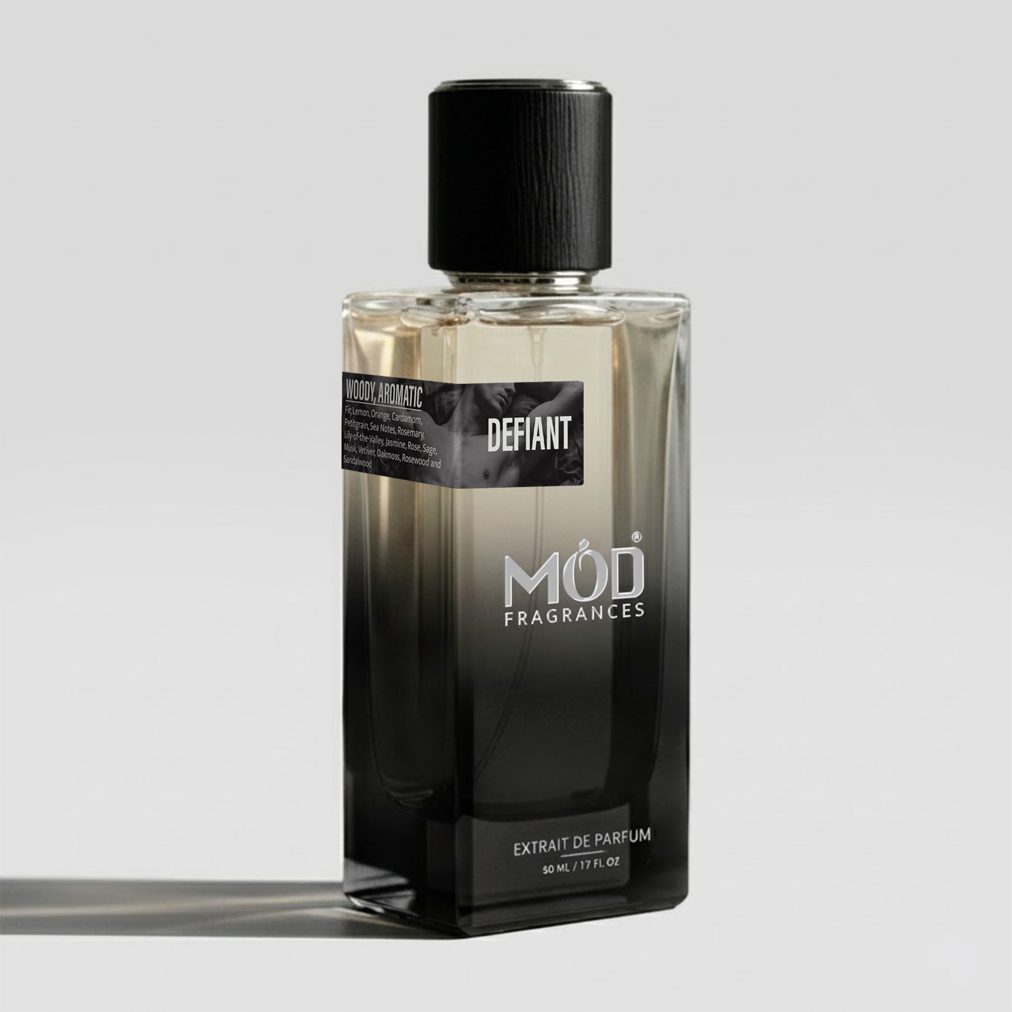 A bottle of Mod Fragrances Defiant Extrait de Parfum, featuring a black-to-clear gradient glass bottle with a black cap, set against a light gray background.