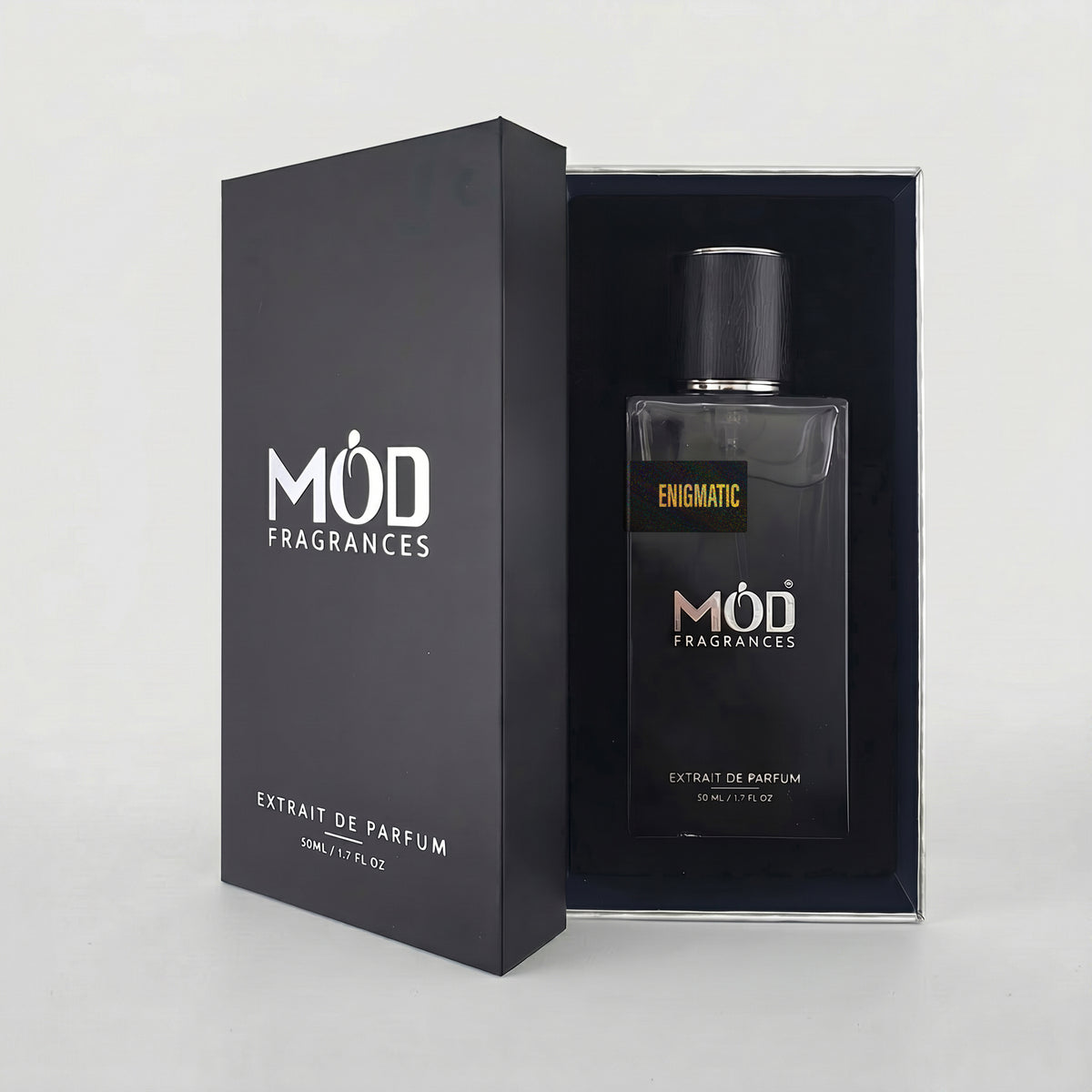 An open premium black perfume box reveals a rectangular glass bottle labeled “Enigmatic” by MOD Fragrances, resting securely in a black-lined presentation case.