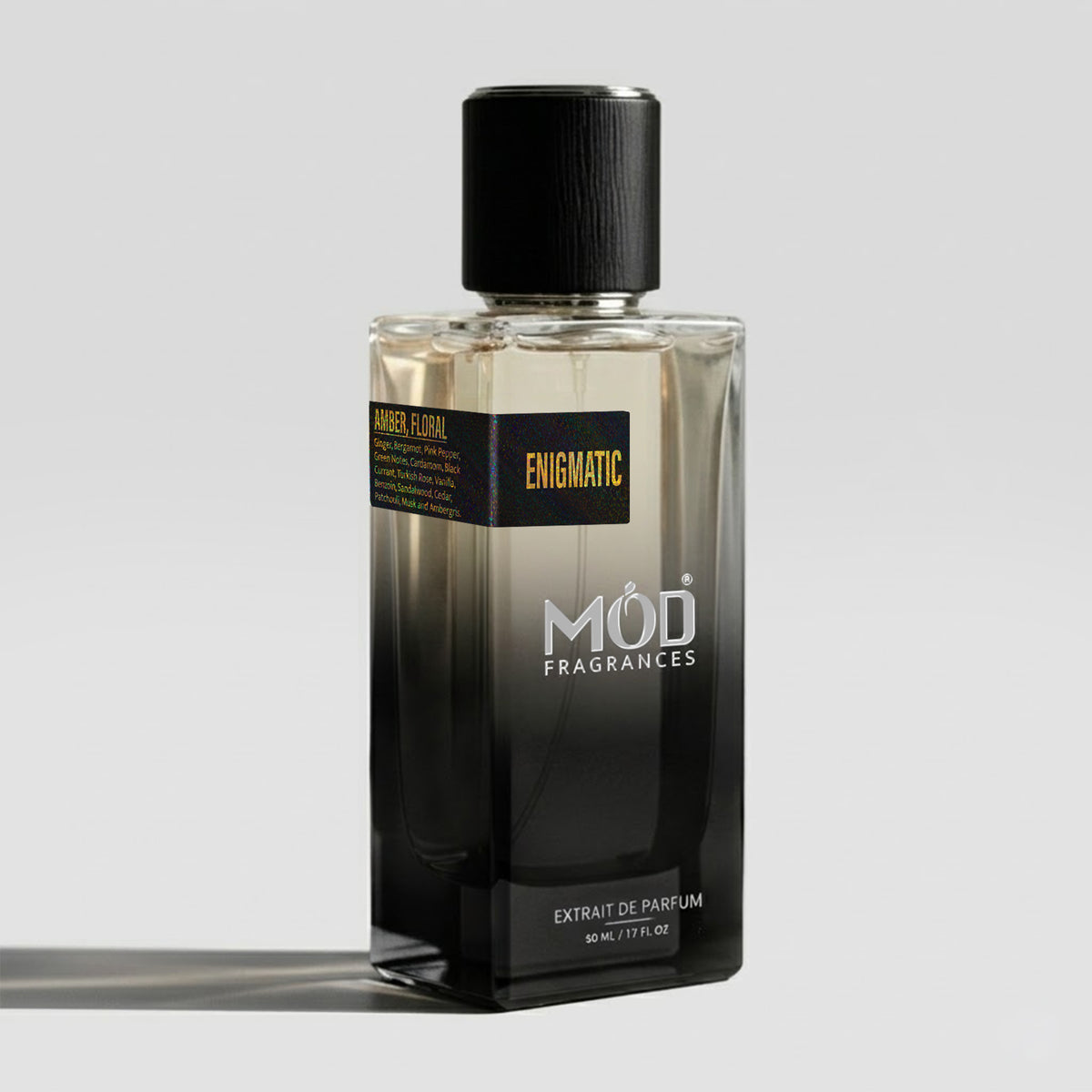 A rectangular glass perfume bottle by MOD Fragrances, labeled “Enigmatic” with a small label detailing its notes, stands on a light background.