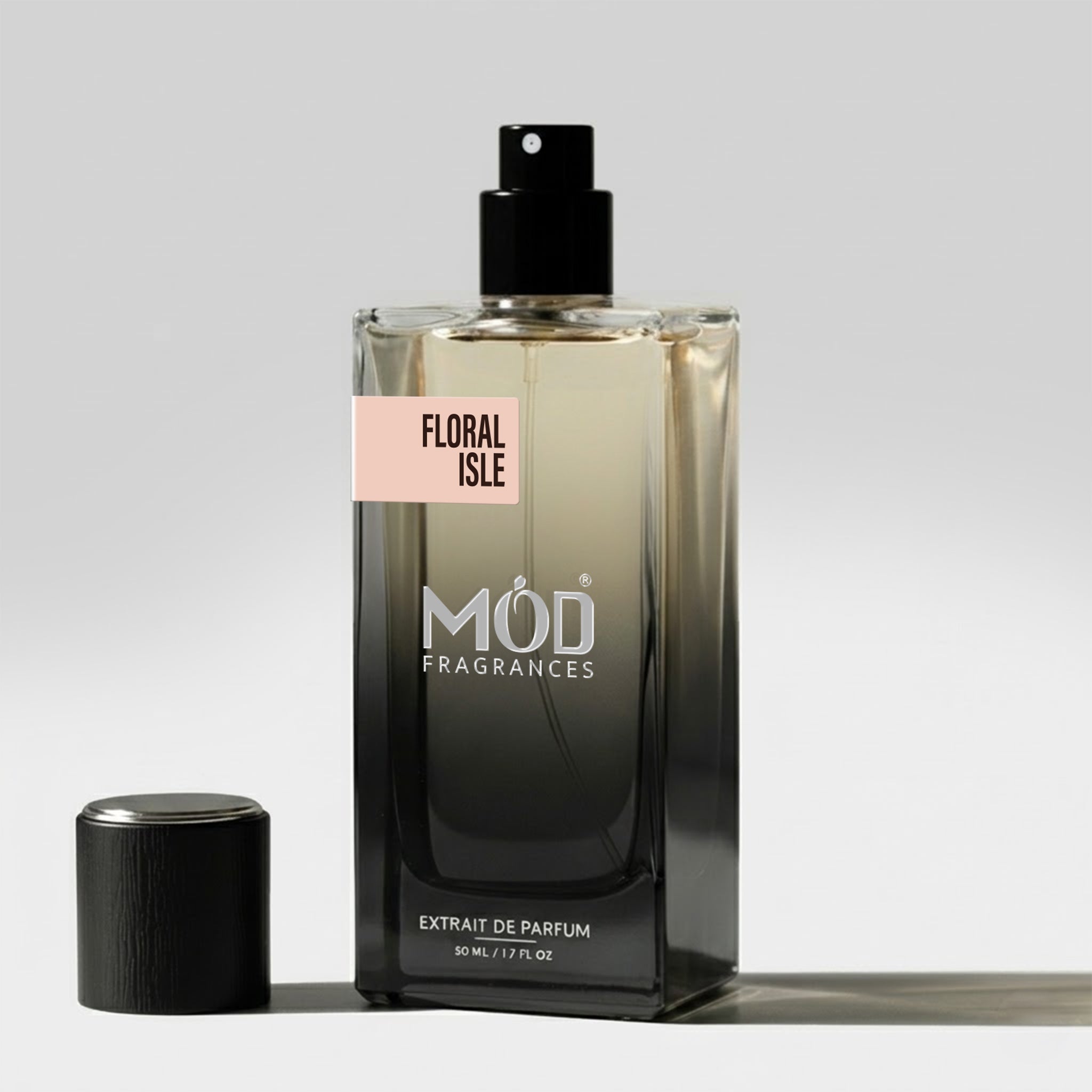 A rectangular glass perfume bottle by MOD Fragrances, labeled "Floral Isle” stands on a light surface with its black cap placed beside it.