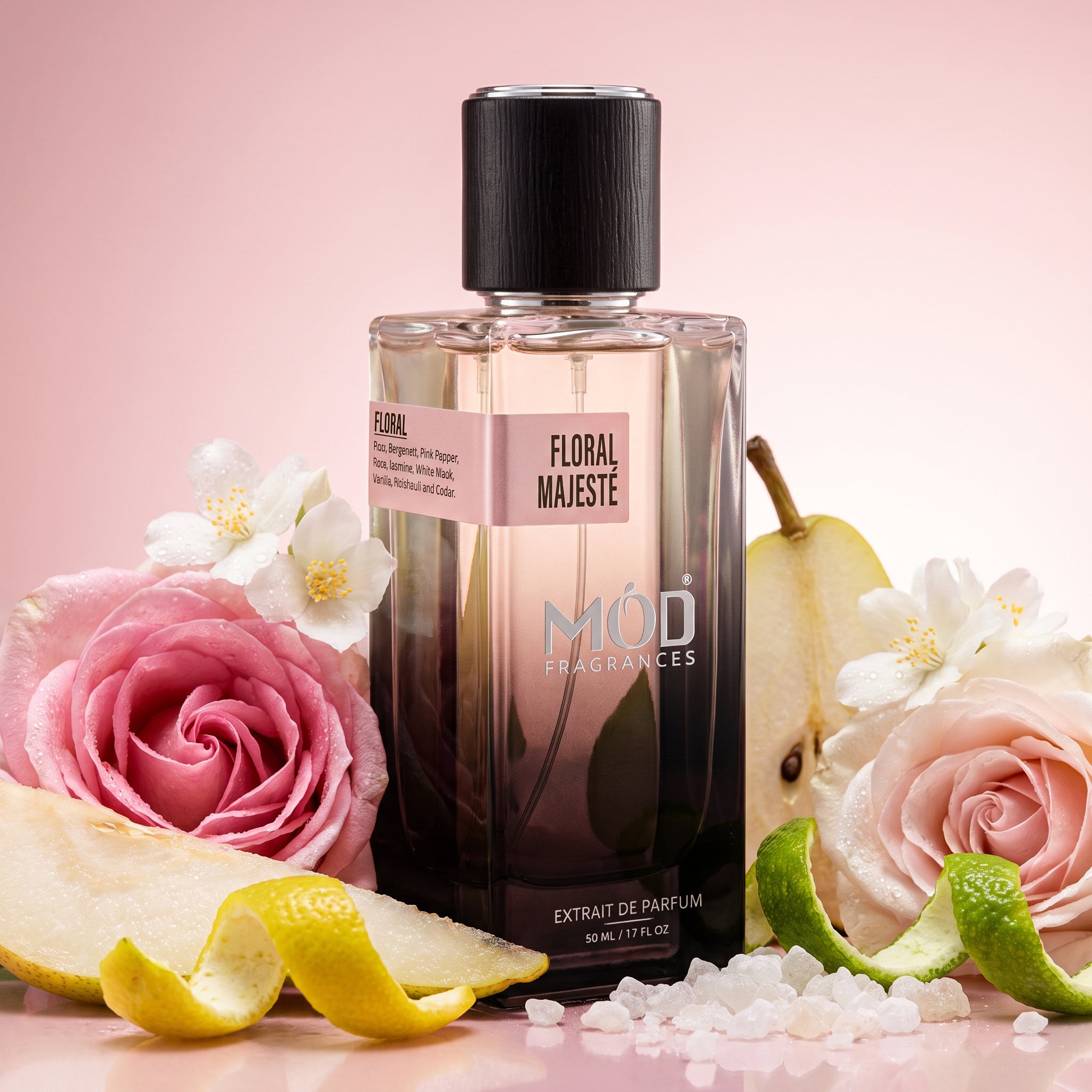 A rectangular glass perfume bottle by MOD Fragrances, labeled "Floral Majeste” is nestled inside its ingredients like bergamot, pears, pink pepper, red rose, vanilla, jasmine, cedar, white musk, on pink background and glossy pink floor.