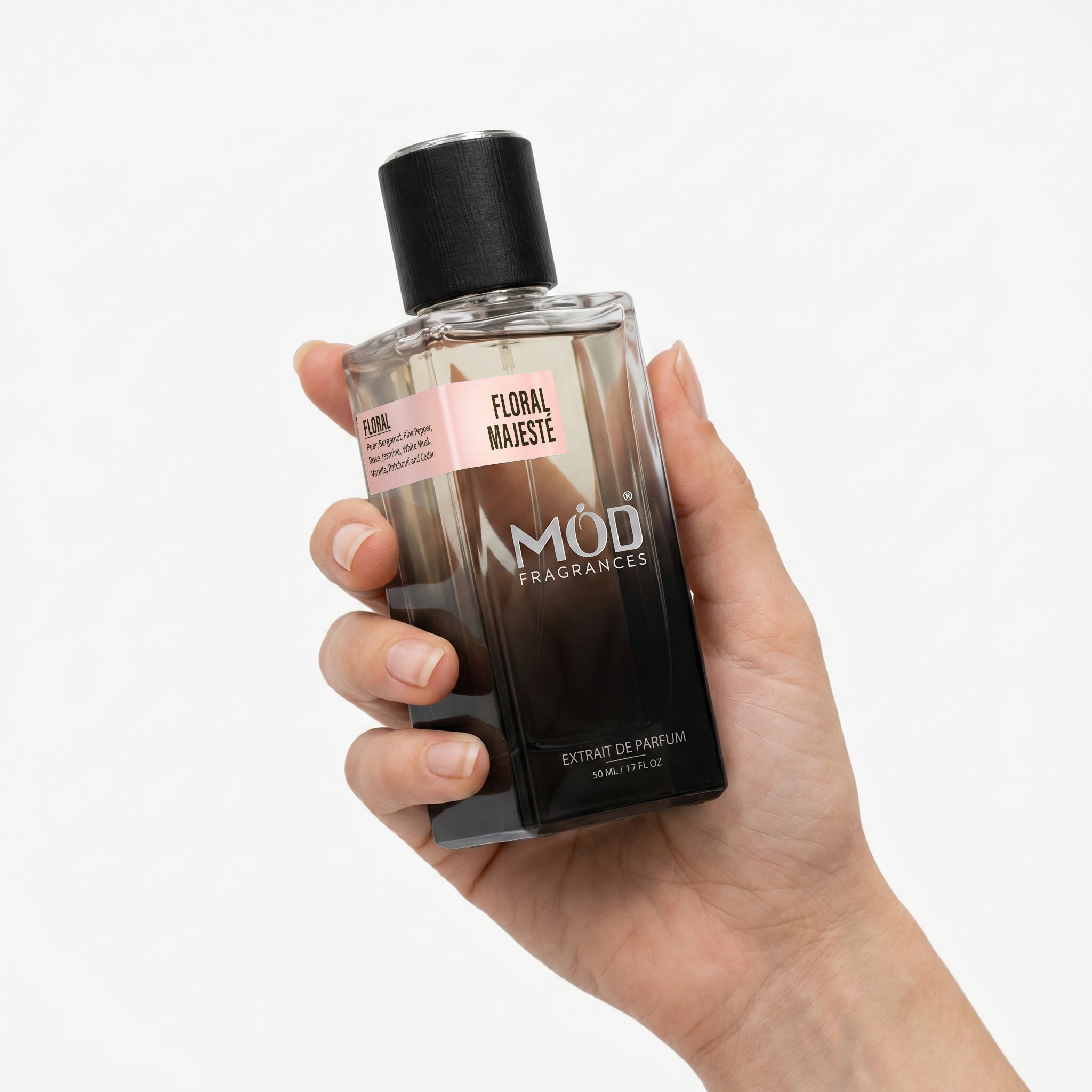 A Female person's hand holds a rectangular glass perfume bottle by MOD Fragrances, labeled "Floral Majeste” against a plain white background.