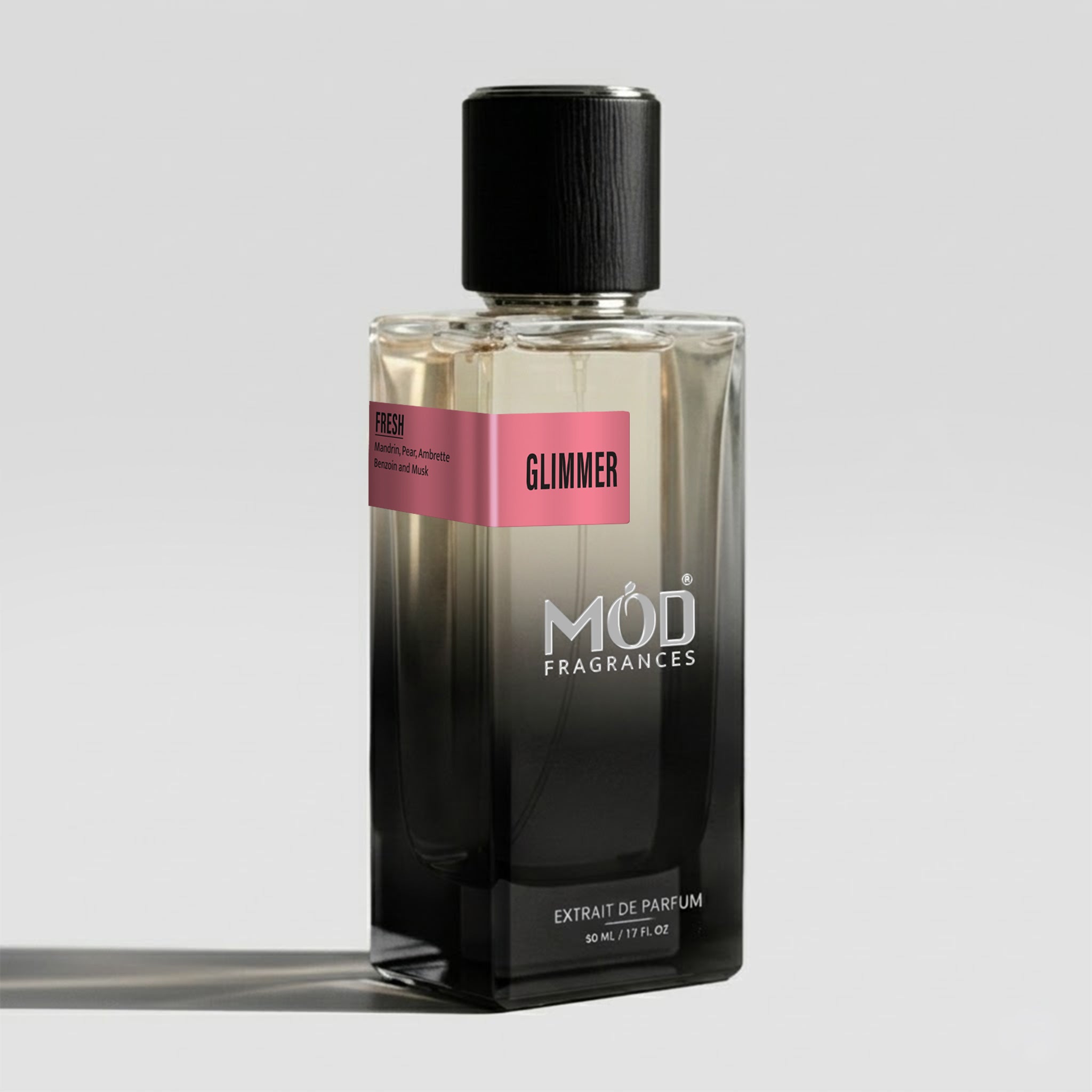 A rectangular glass perfume bottle by MOD Fragrances, labeled “Glimmer” with a small label detailing its leather, woody notes, stands on a light background.