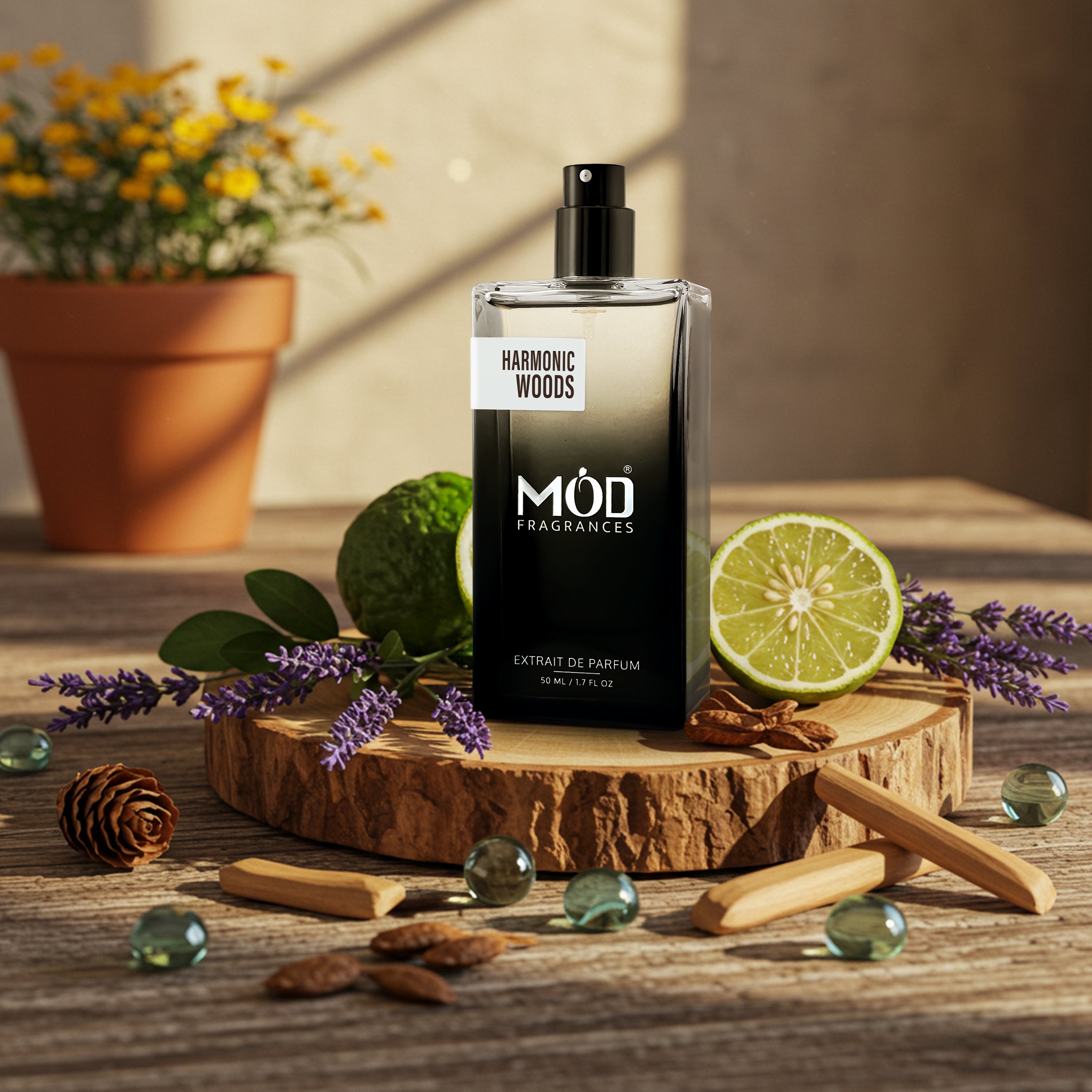 A perfume bottle labeled 'HARMONIC WOODS' by 'MÓD FRAGRANCES' stands on a rustic wooden slice with sliced lime, lavender sprigs, cinnamon sticks, and green stones on a wooden table. A potted yellow flower sits blurred in the background.