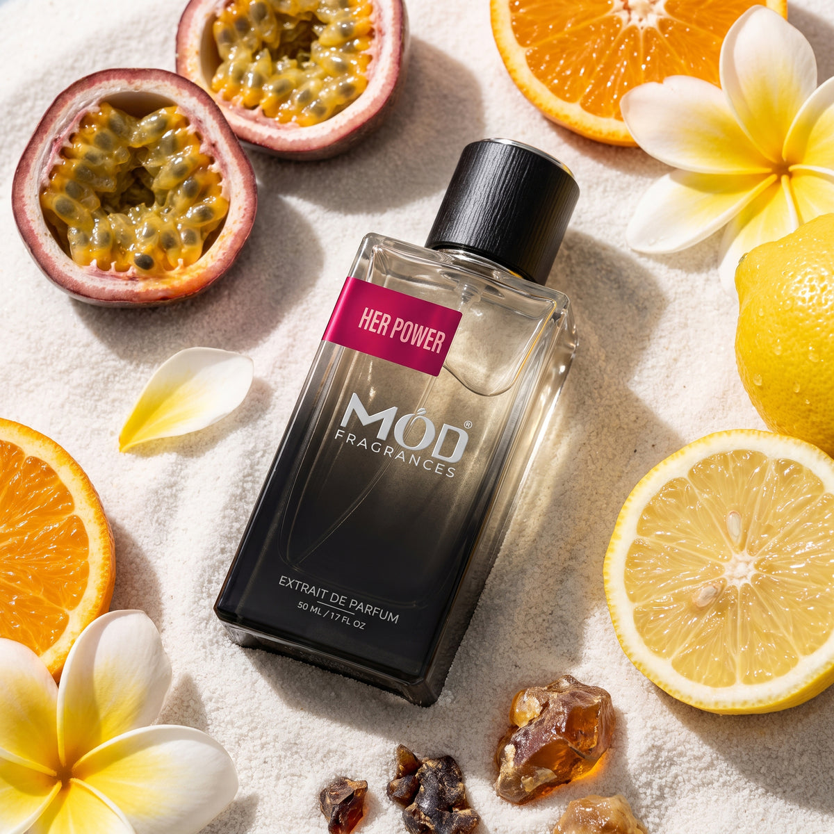 A bottle of MOD FRAGRANCES 'Her Power' extrait de parfum is styled in a flat-lay arrangement on a textured white surface, surrounded by citrus slices (orange, lemon), halved passion fruits, and white plumeria flowers.