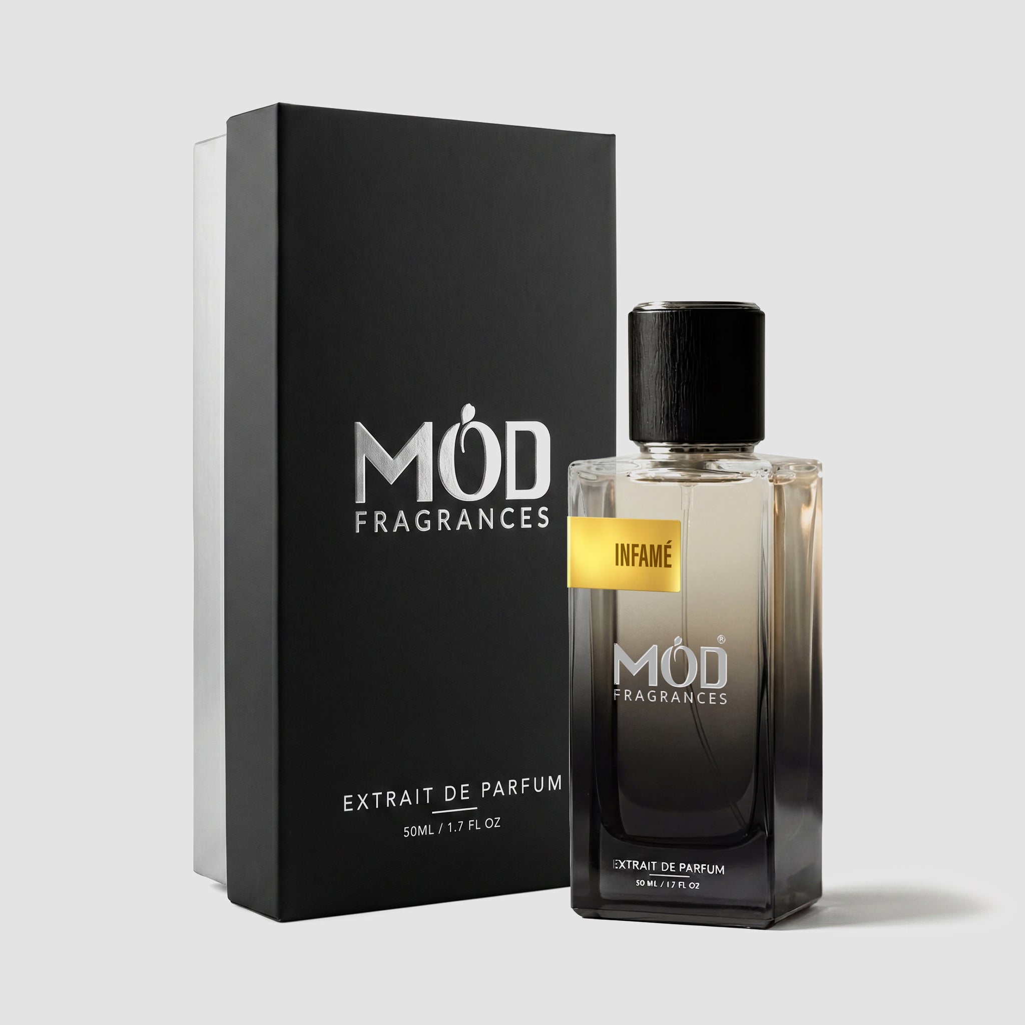 A rectangular perfume bottle by MOD Fragrances, labeled “Infame” is positioned next to its closed, upright premium black display box on a light grey background.