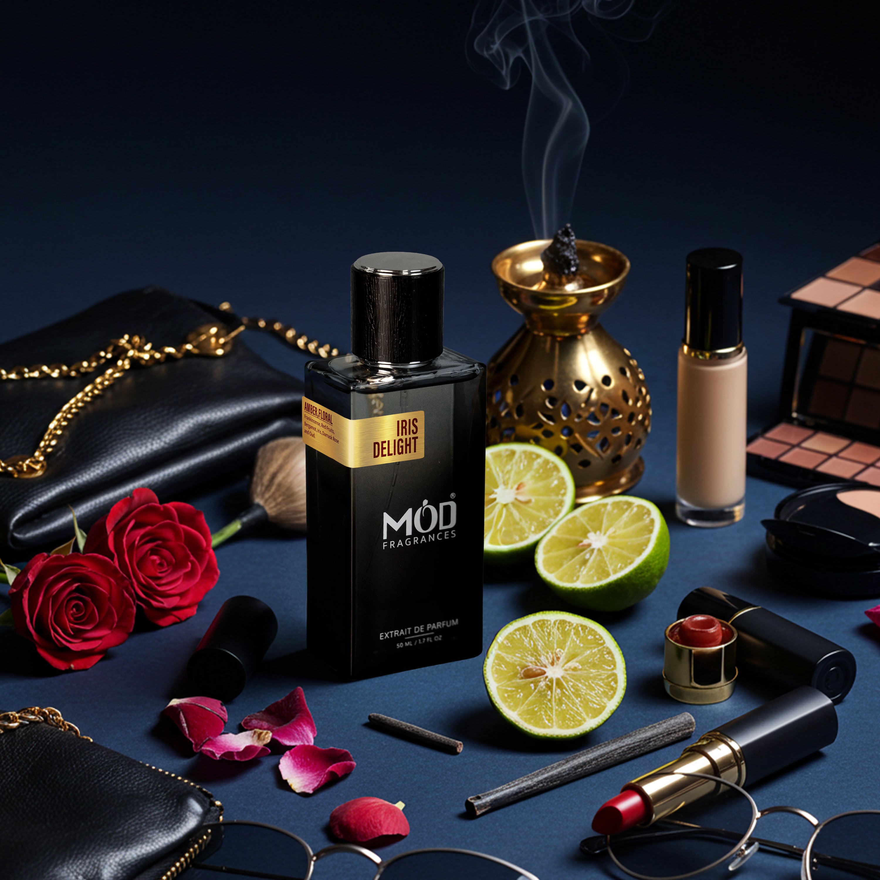 A perfume bottle labeled MOD FRAGMENTS IRIS DELIGHT stands on a dark blue surface surrounded by cosmetics, red roses, lime halves, a gold incense burner, sunglasses, and other beauty props.