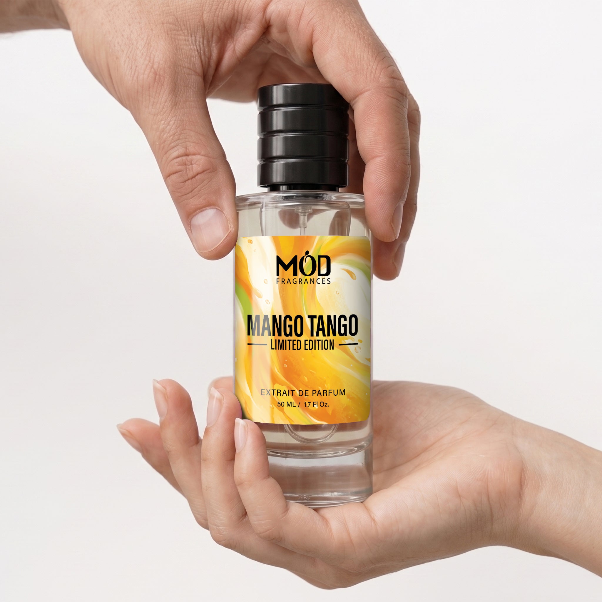 A hand holds a clear glass perfume bottle labeled 'MÓD Fragrances Mango Tango Limited Edition' against a clean white background.