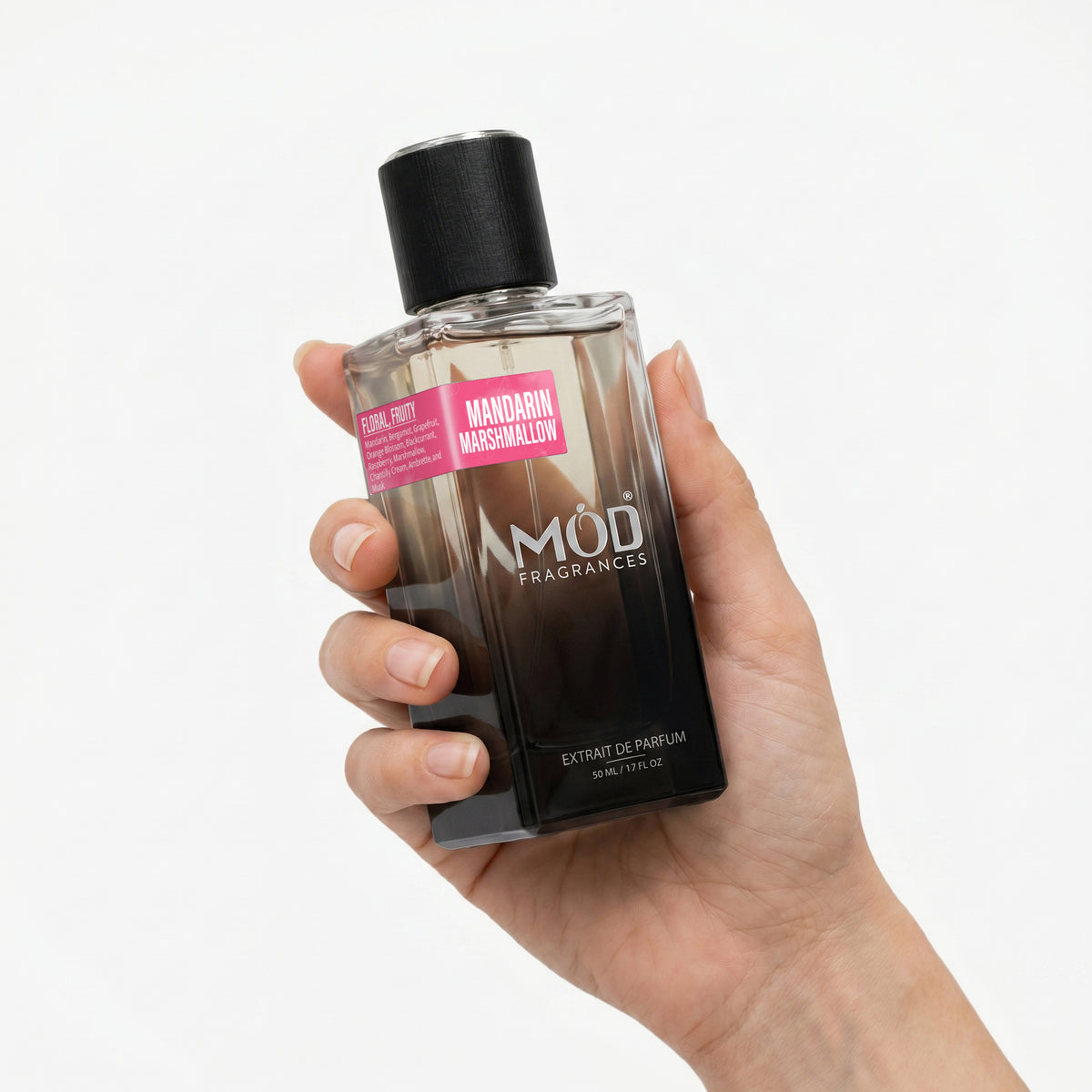 A hand holding a bottle of MOD Fragrances Extrait de Parfum in the Mandarin Marshmallow scent, set against a plain white background.