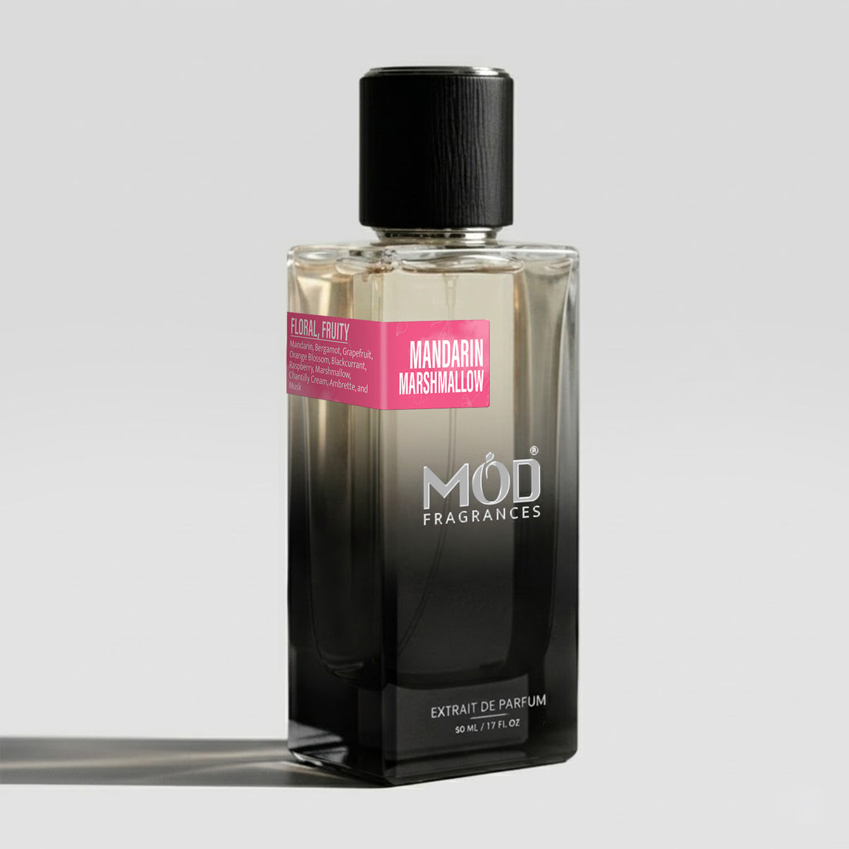 A bottle of MOD Fragrances 'Mandarin Marshmallow' extrait de parfum, featuring a black-to-clear gradient glass bottle with a black cap and a pink label, set against a light gray background.