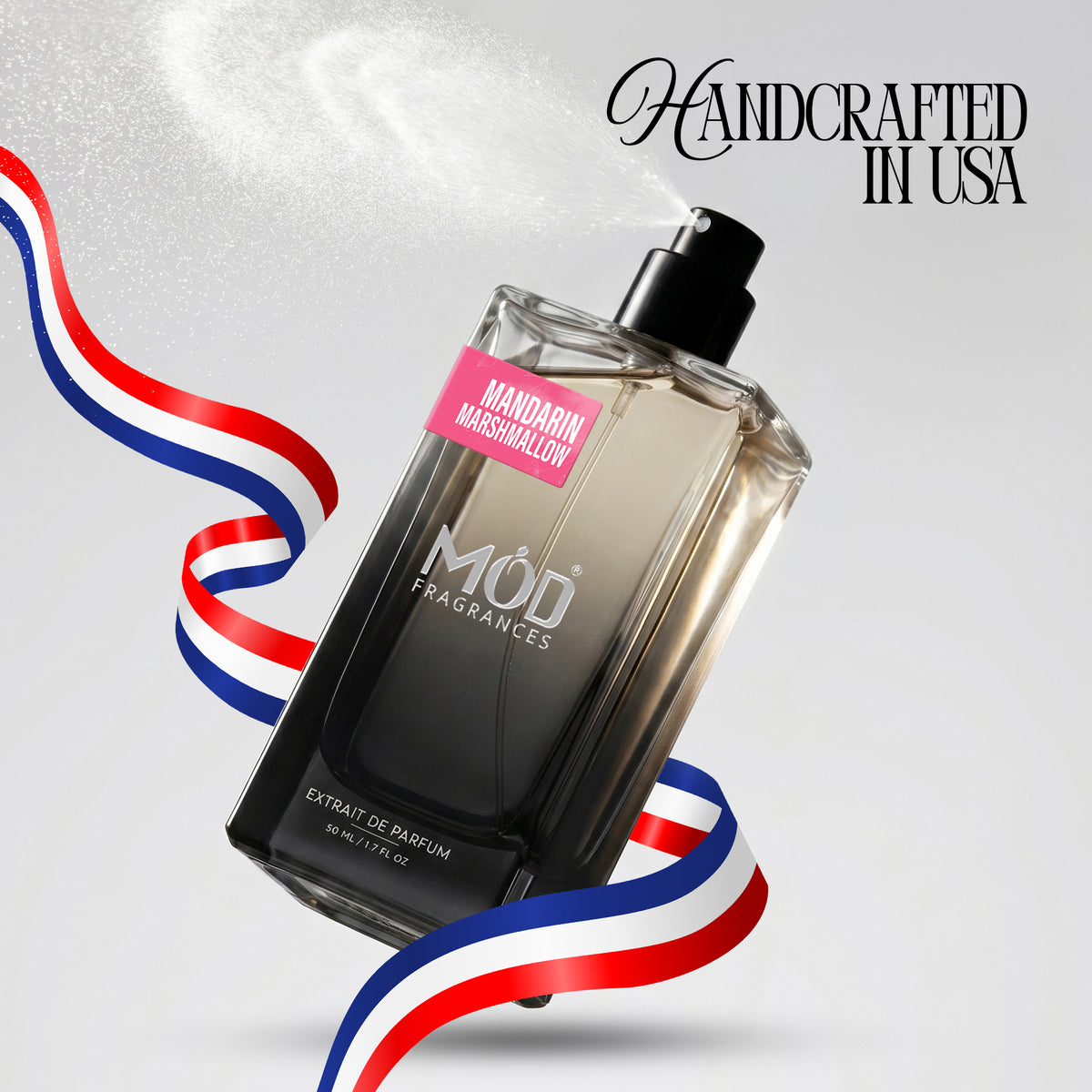 A bottle of MOD Fragrances Mandarin Marshmallow extrait de parfum floating diagonally on a light gray background with red, white, and blue ribbon graphics and the text 'Handcrafted in USA'.