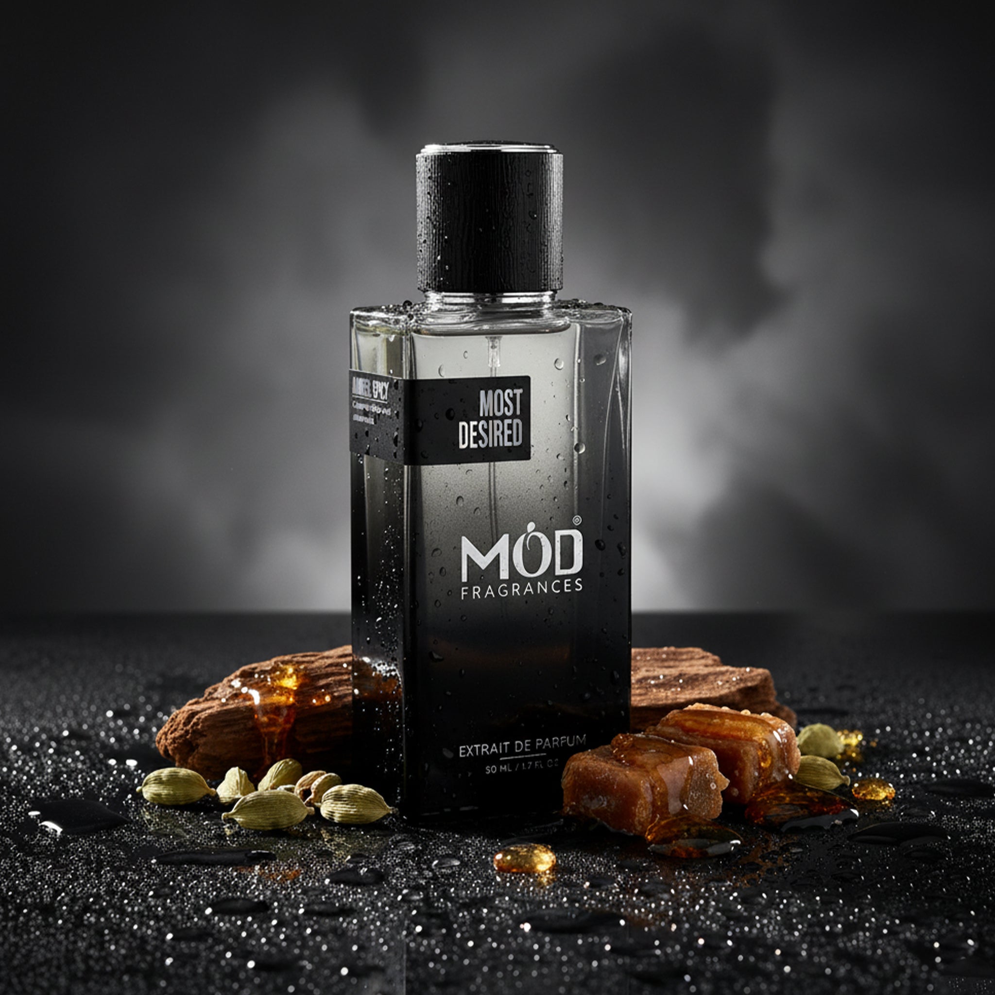 A rectangular glass perfume bottle by MOD Fragrances, labeled "Most Desired" is standing between cardamom, toffee, amber and woods, placed on dark black wet moist surface, on a dense foggy smokey dark background.