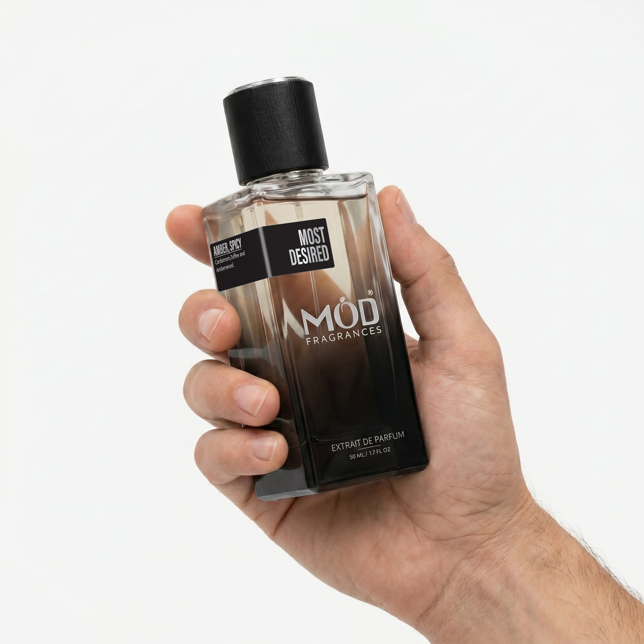 A male person's hand holds a rectangular glass perfume bottle by MOD Fragrances, labeled "Most Desired" against a plain white background.