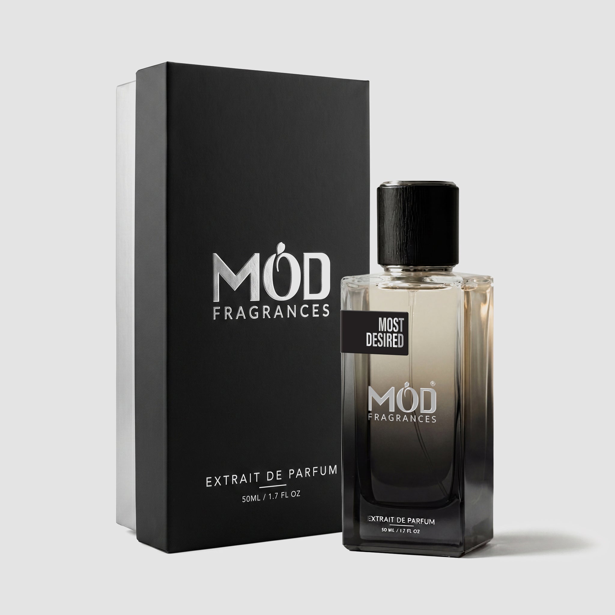 A rectangular perfume bottle by MOD Fragrances, labeled “Most Desired” is positioned next to its closed, upright premium black display box on a light grey background.