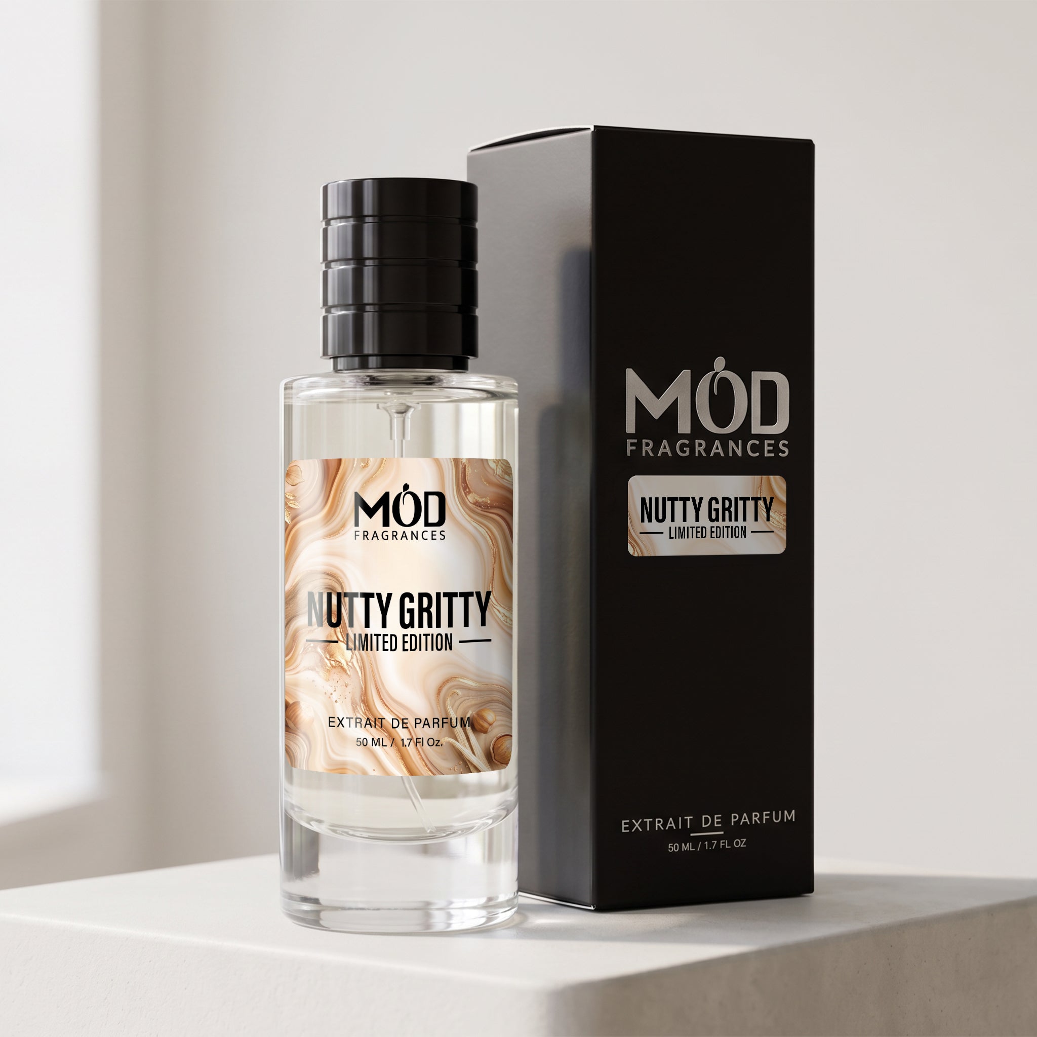 A bottle of MÓD Fragrances 'Nutty Gritty' limited edition extrait de parfum stands next to its black packaging box on a light gray surface.