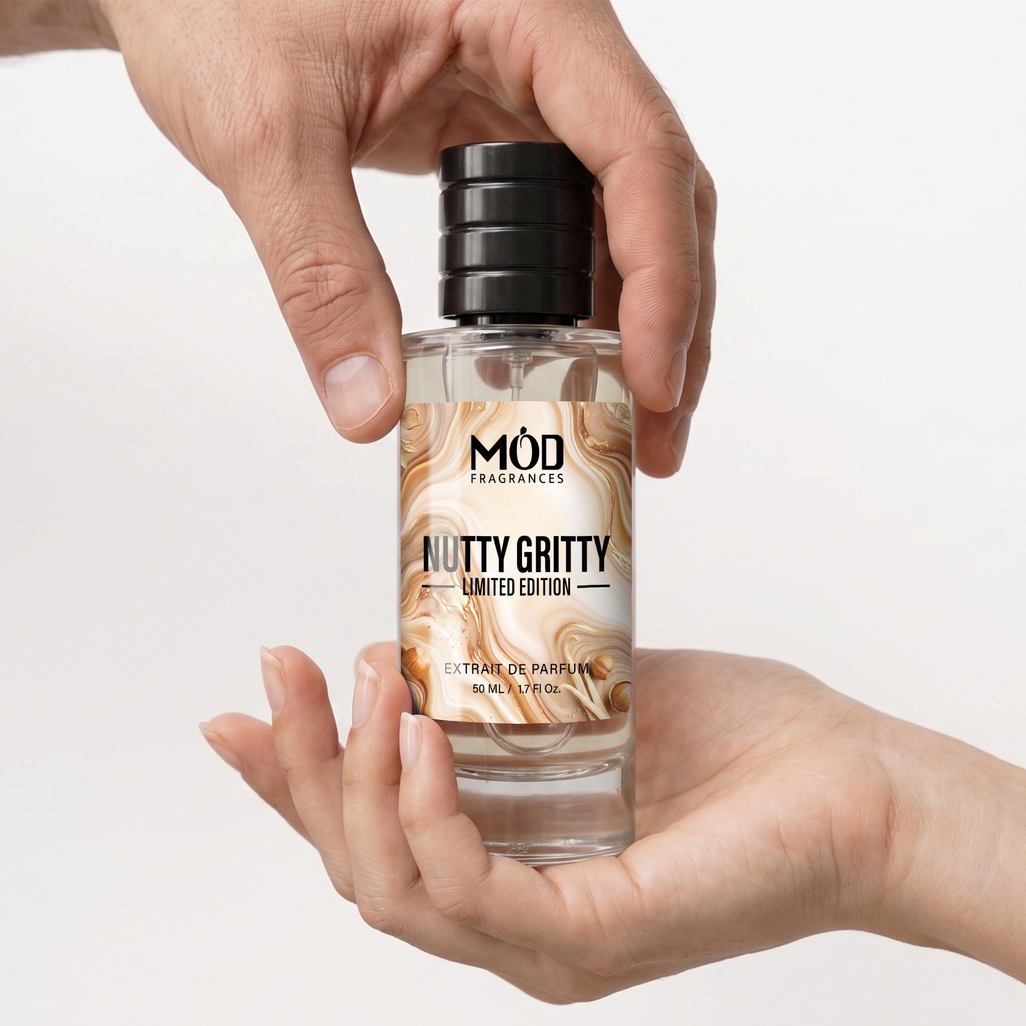 A clear bottle of MOD Fragrances 'Nutty Gritty' Limited Edition extra virgin perfume, held in two hands against a clean white background.