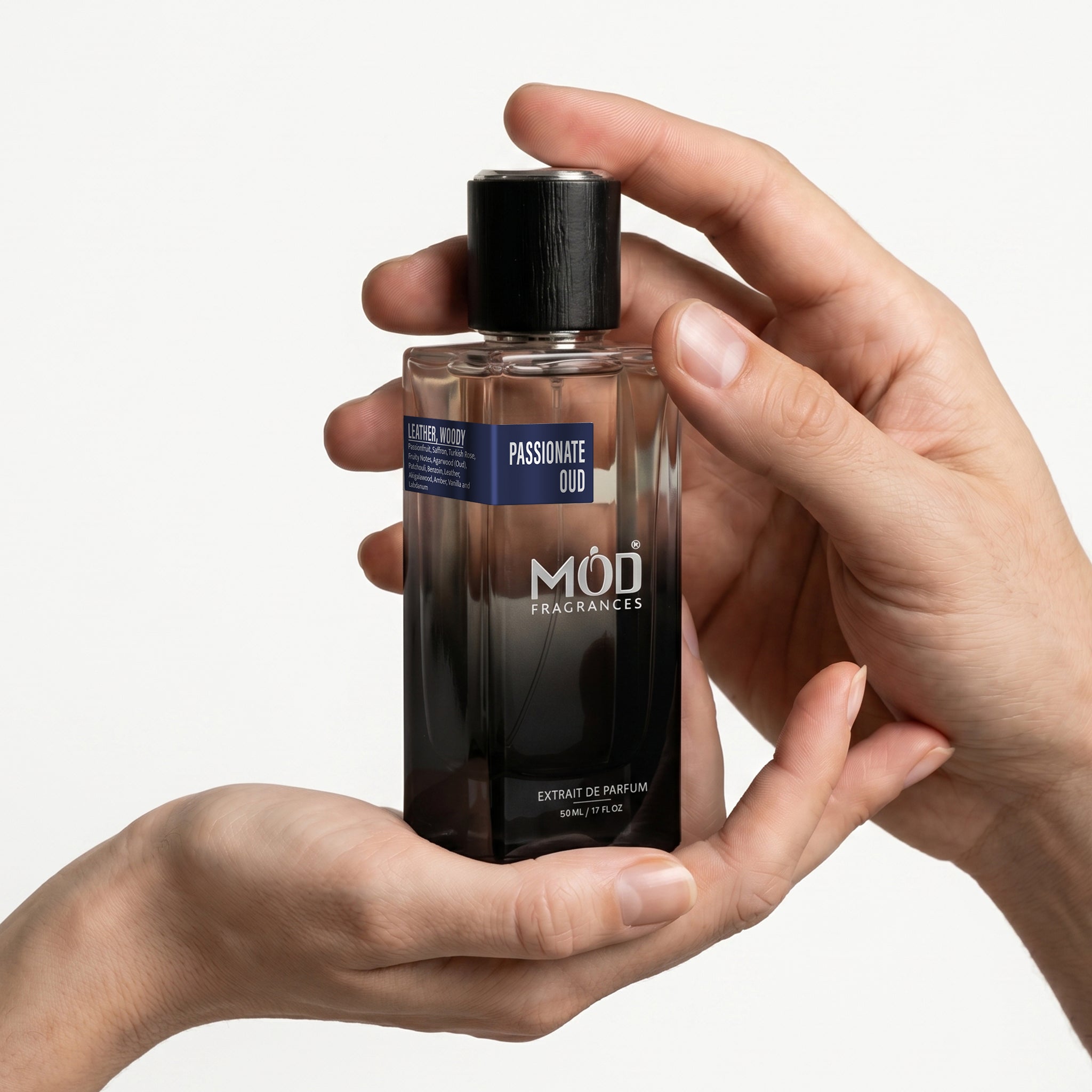 A male and a female person's hand holds a rectangular glass perfume bottle by MOD Fragrances, labeled "Passionate Oud" against a plain white background.