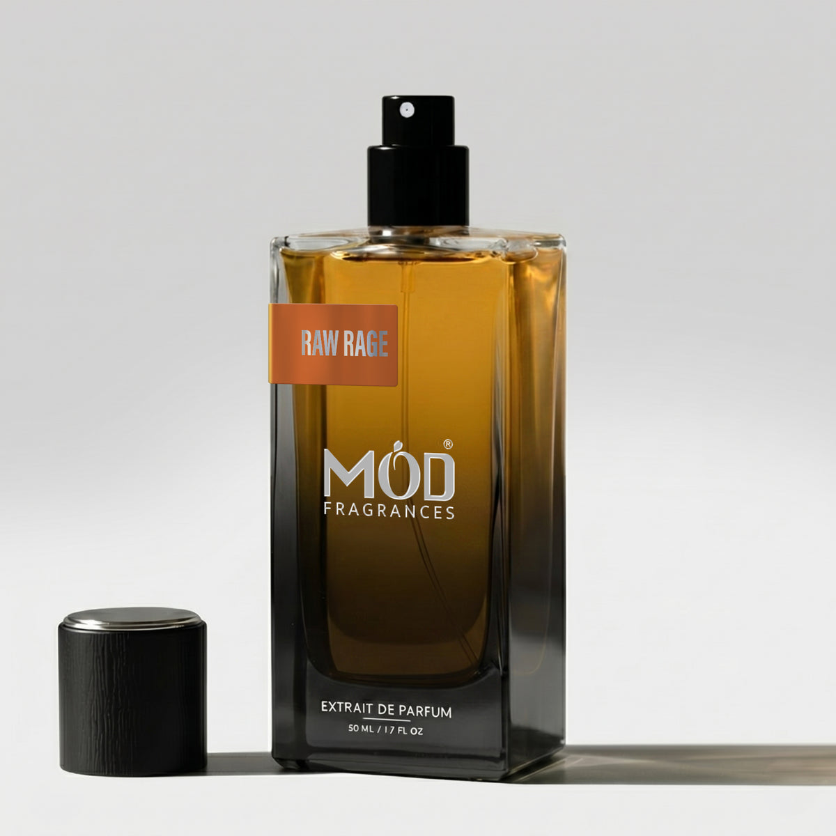 A rectangular glass perfume bottle by MOD Fragrances, labeled "Raw Rage” stands on a light surface with its black cap placed beside it.