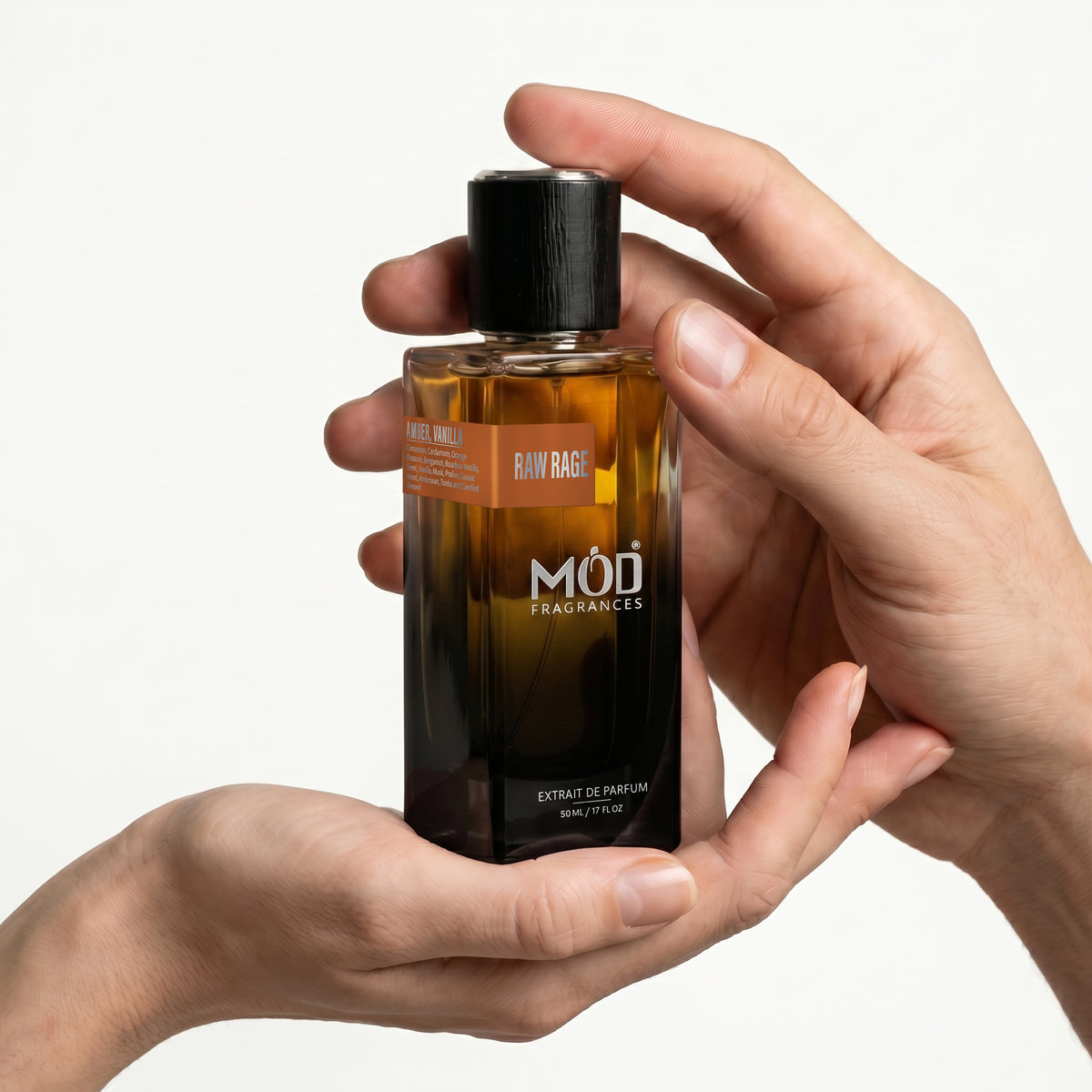 A Male and a female person's hand holds a rectangular glass perfume bottle by MOD Fragrances, labeled "Raw Rage” against a plain white background.