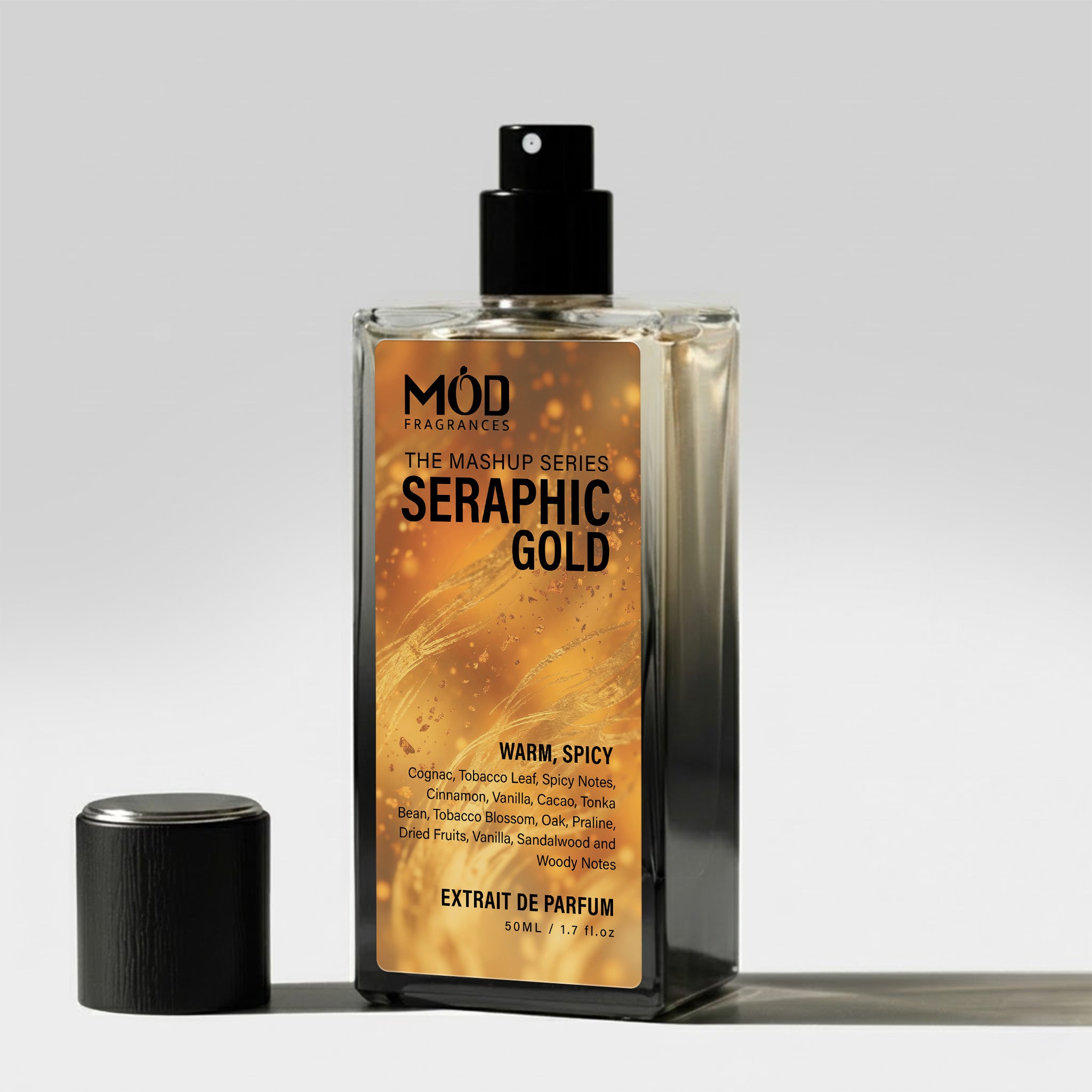 A rectangular glass perfume bottle by MOD Fragrances, labeled "Mashup series Seraphic Gold" stands on a light surface with its black cap placed beside it.