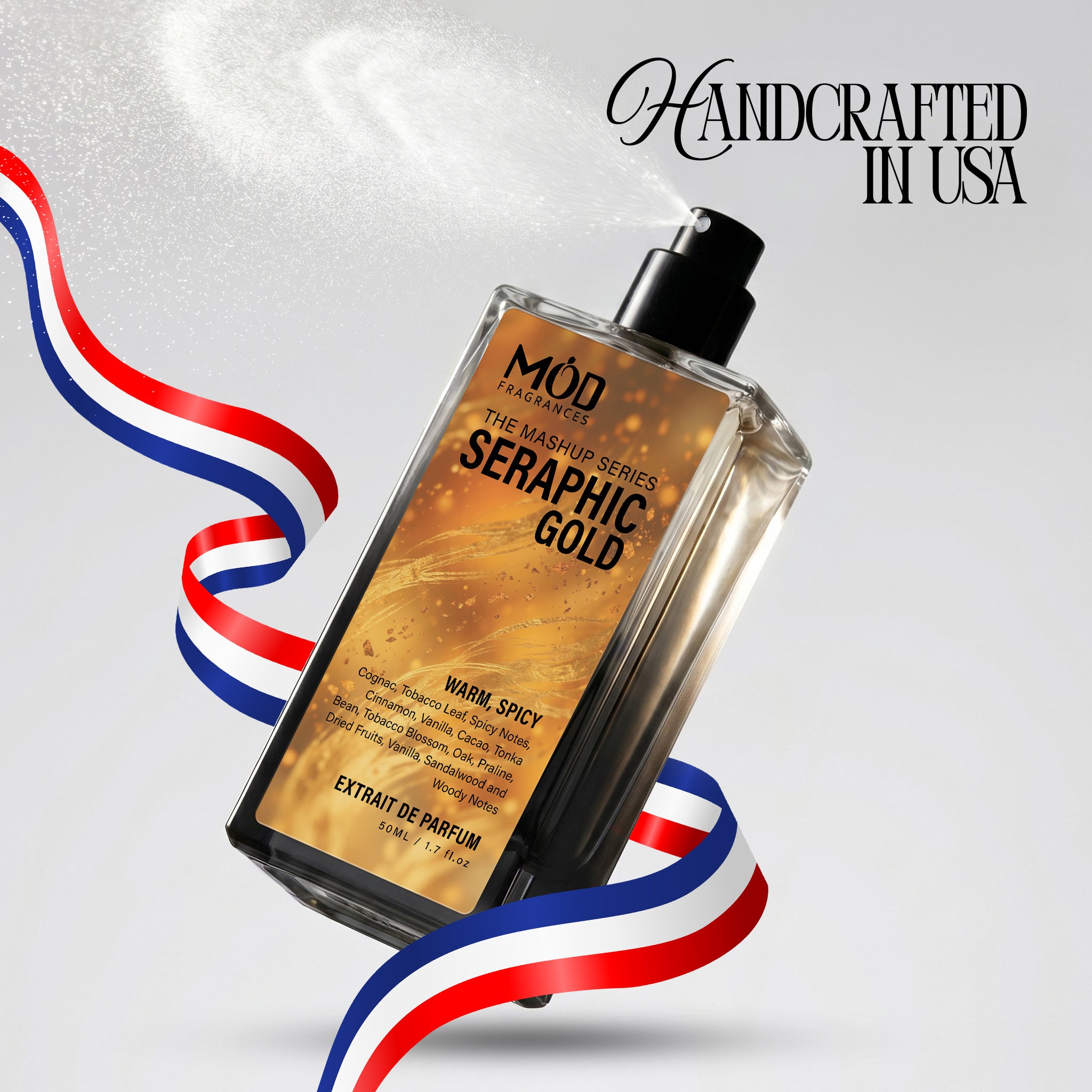 A rectangular glass perfume bottle by MOD Fragrances, labeled "Mashup series Seraphic Gold" is captured mid-spray with a fine mist dispersing into the air, accented by stylized red, white, and blue ribbons, with the text "Handcrafted in USA" in the upper right.