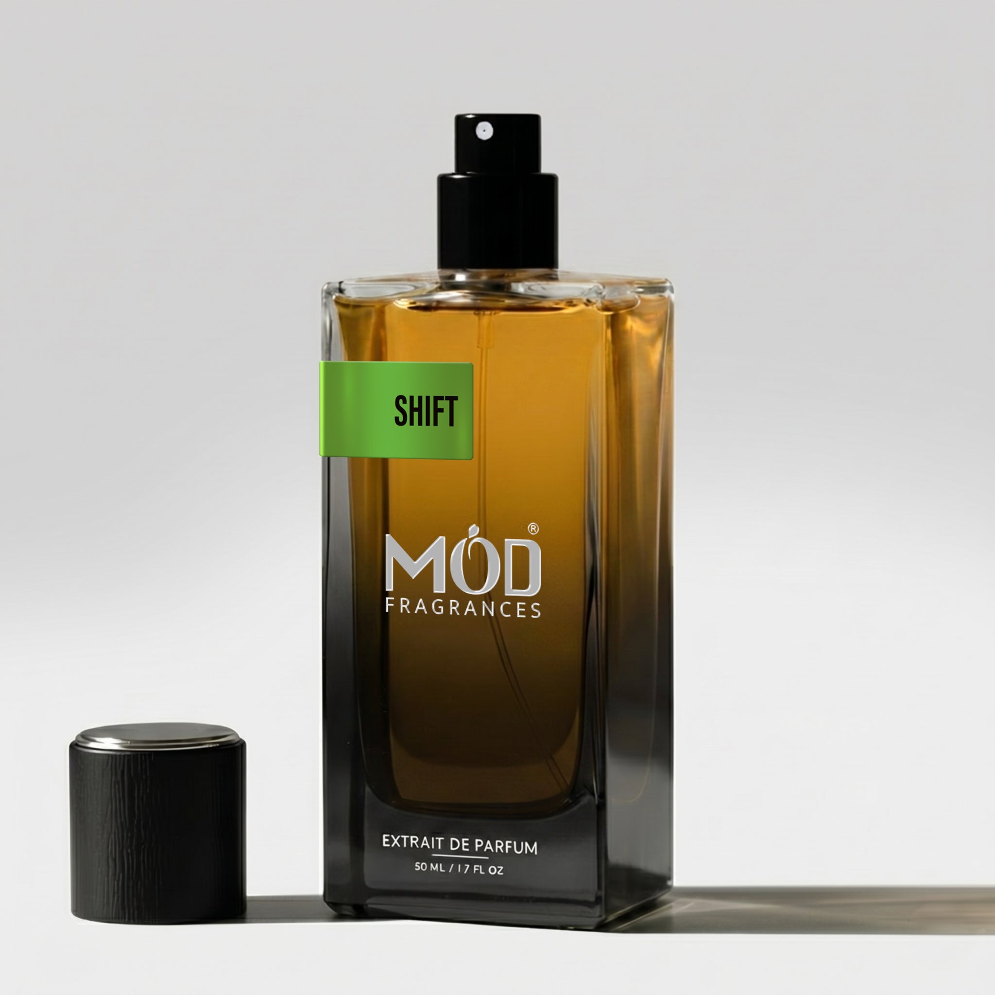 A rectangular glass perfume bottle by MOD Fragrances, labeled "Shift" stands on a light surface with its black cap placed beside it.