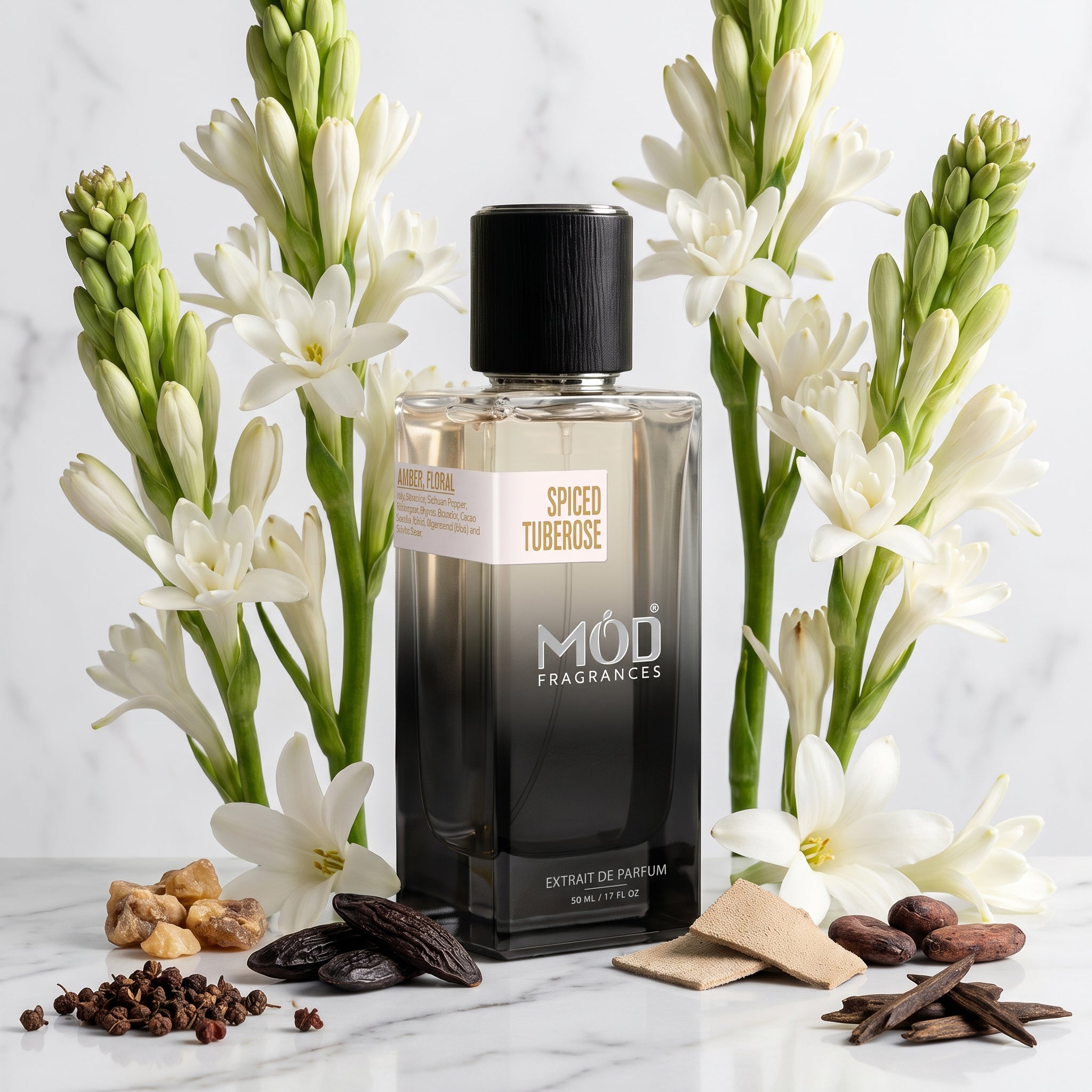 A rectangular glass perfume bottle by MOD Fragrances, labeled "Spiced Tuberose" is nestled between its ingredients like Sichuan pepper, tuberose, jasmine, lily, styrax, benzoin, tonic beans, suede, cacao, agarwood, on white and grey vein marble with same white marble background