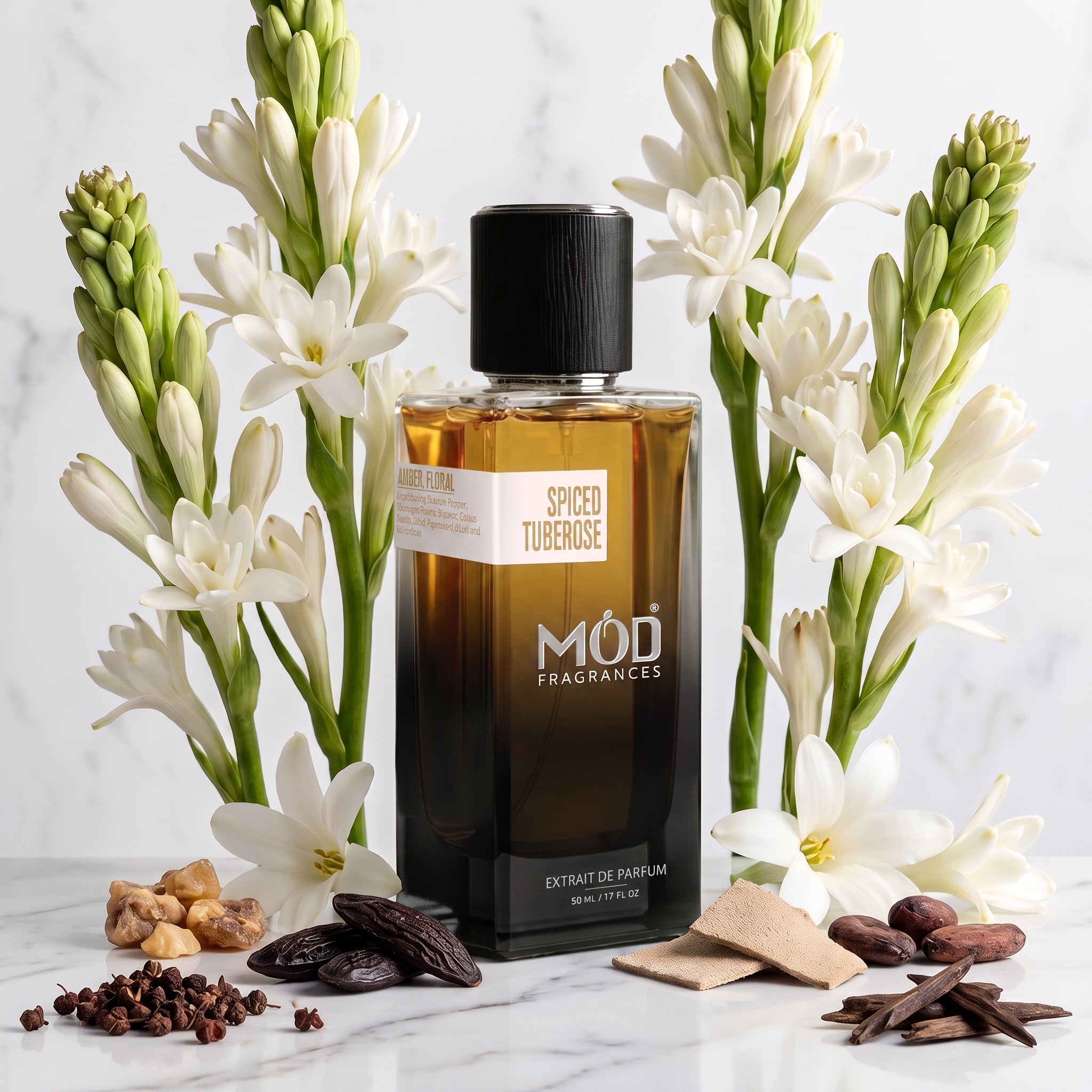 A rectangular glass perfume bottle by MOD Fragrances, labeled "Spiced Tuberose" is nestled between its ingredients like Sichuan pepper, tuberose, jasmine, lily, styrax, benzoin, tonic beans, suede, cacao, agarwood, on white and grey vein marble with same white marble background
