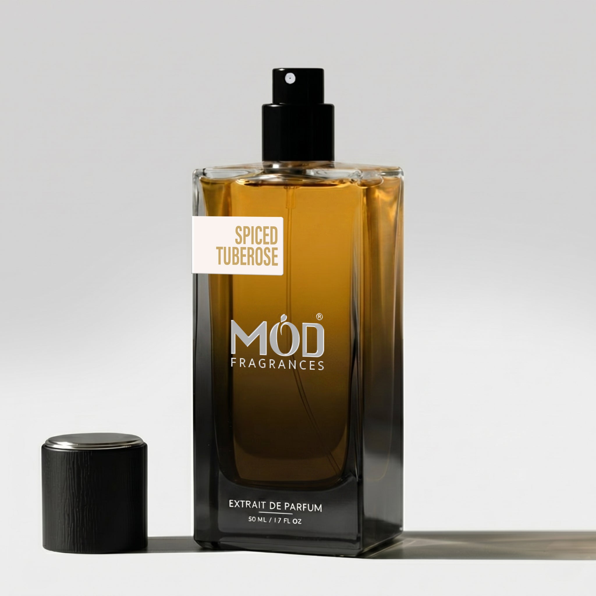 A rectangular glass perfume bottle by MOD Fragrances, labeled "Spiced Tuberose" stands on a light surface with its black cap placed beside it. 