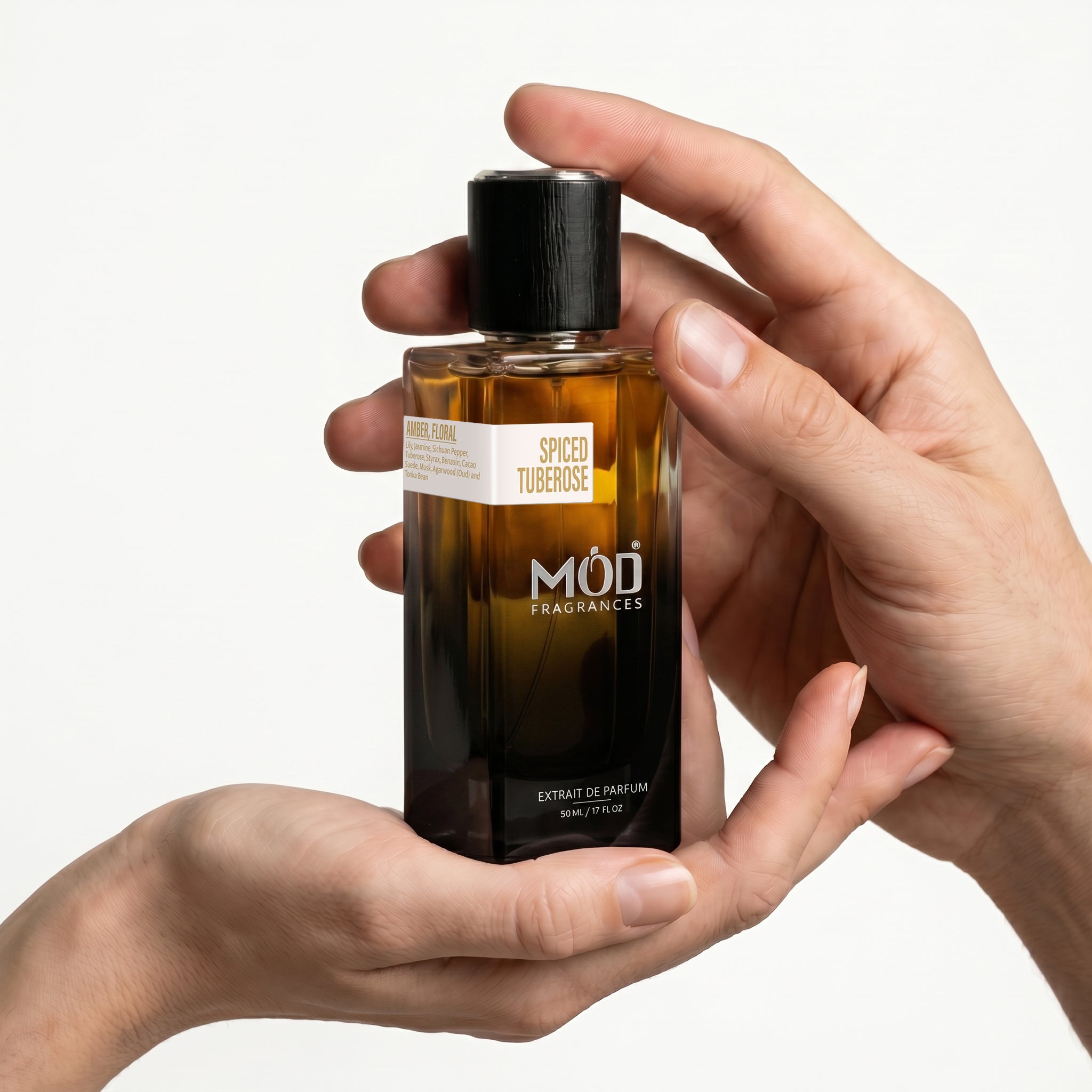 A male & Female person's hand holds a rectangular glass perfume bottle by MOD Fragrances, labeled "Spiced Tuberose" against a plain white background.