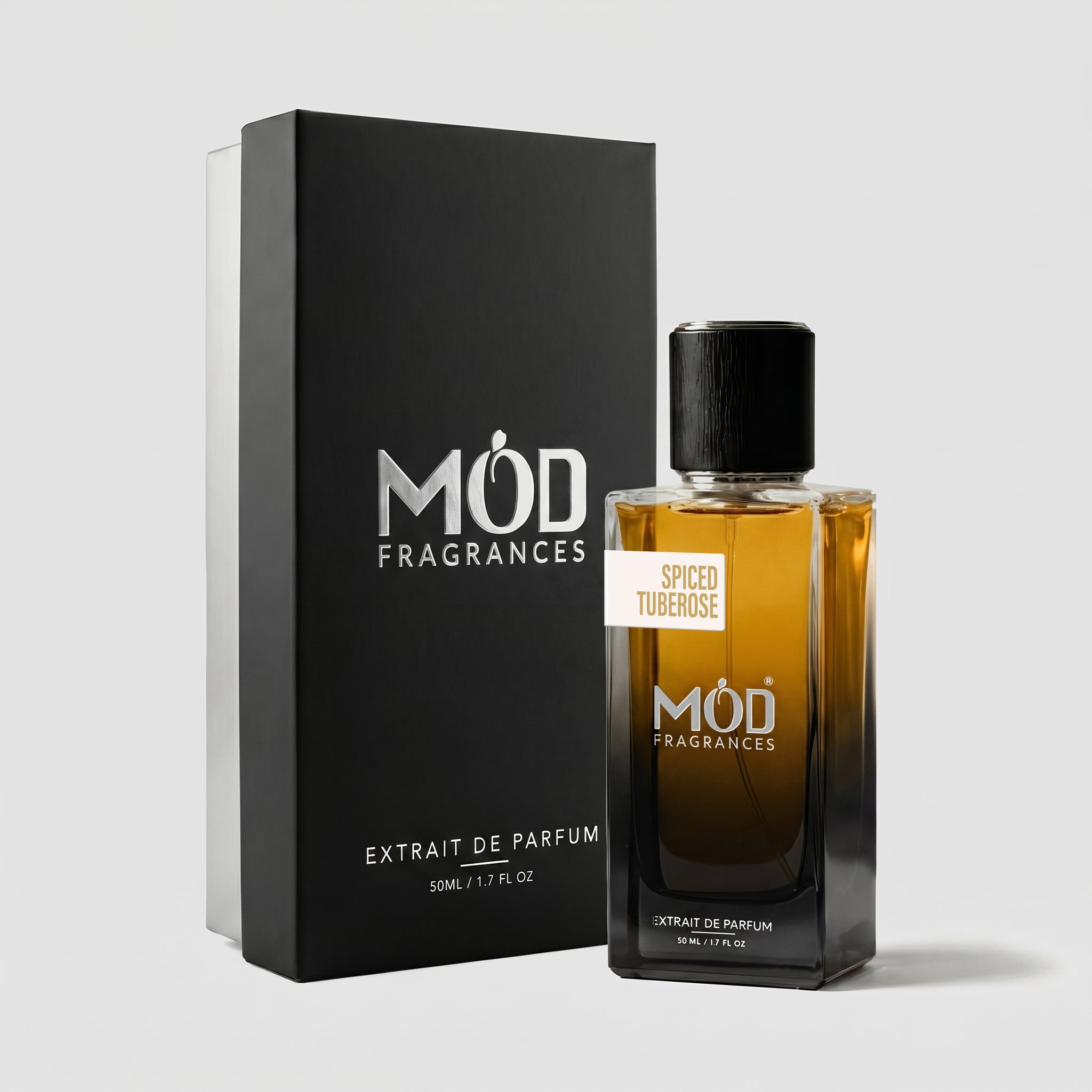 A rectangular perfume bottle by MOD Fragrances, labeled “Spiced Tuberose” is positioned next to its closed, upright premium black display box on a light grey background.