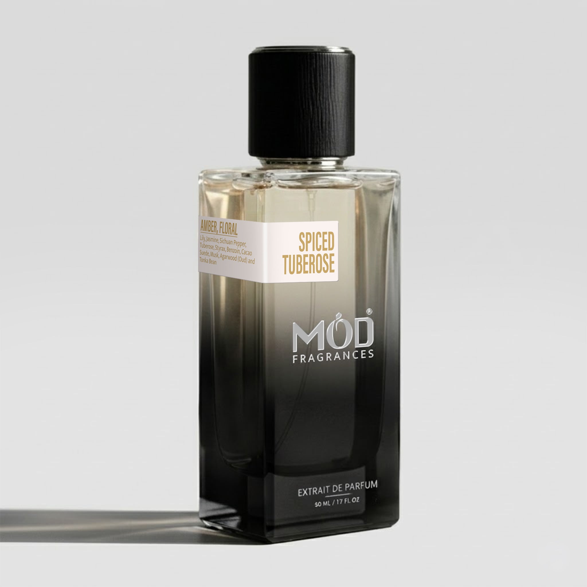 A rectangular glass perfume bottle by MOD Fragrances, labeled “Spiced Tuberose” with a small label detailing its notes, stands on a light background. 