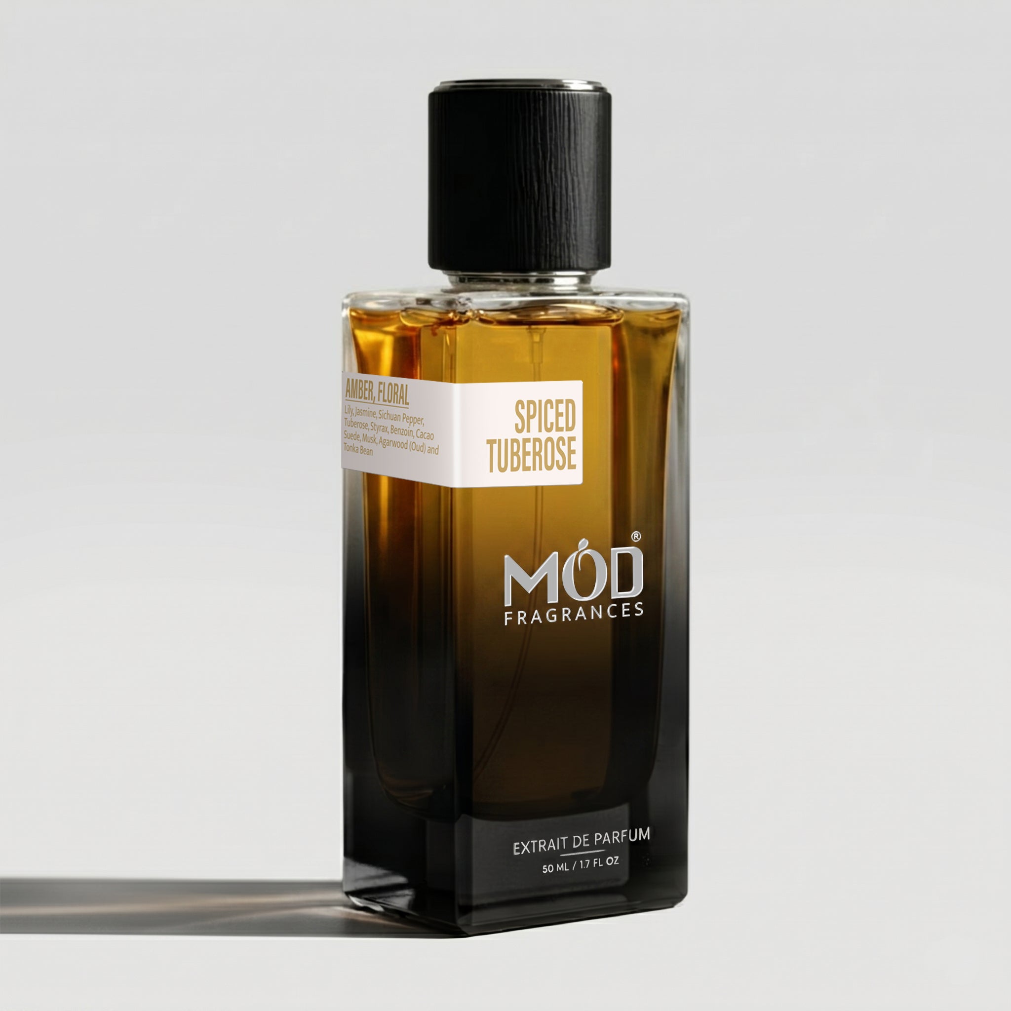 A rectangular glass perfume bottle by MOD Fragrances, labeled “Spiced Tuberose” with a small label detailing its notes, stands on a light background. 