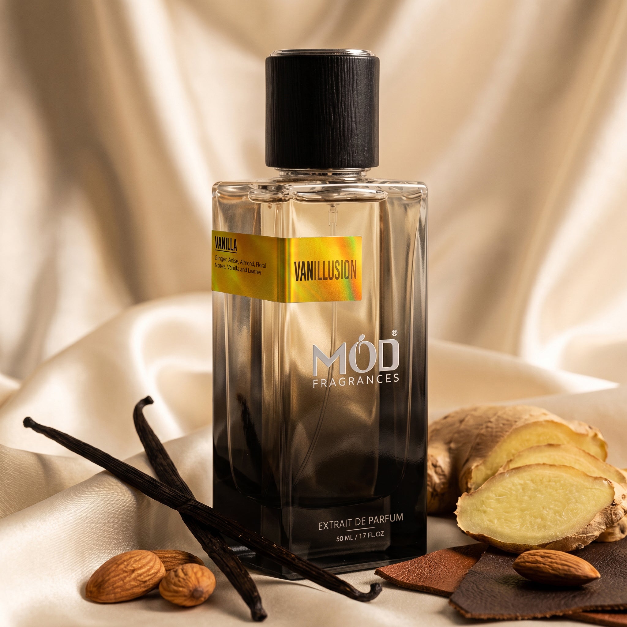 A bottle of Mod Fragrances Vanillion perfume with a black cap and a yellow-to-orange gradient label, styled on draped beige satin with vanilla beans, ginger root, almonds, and a slice of brown leather.